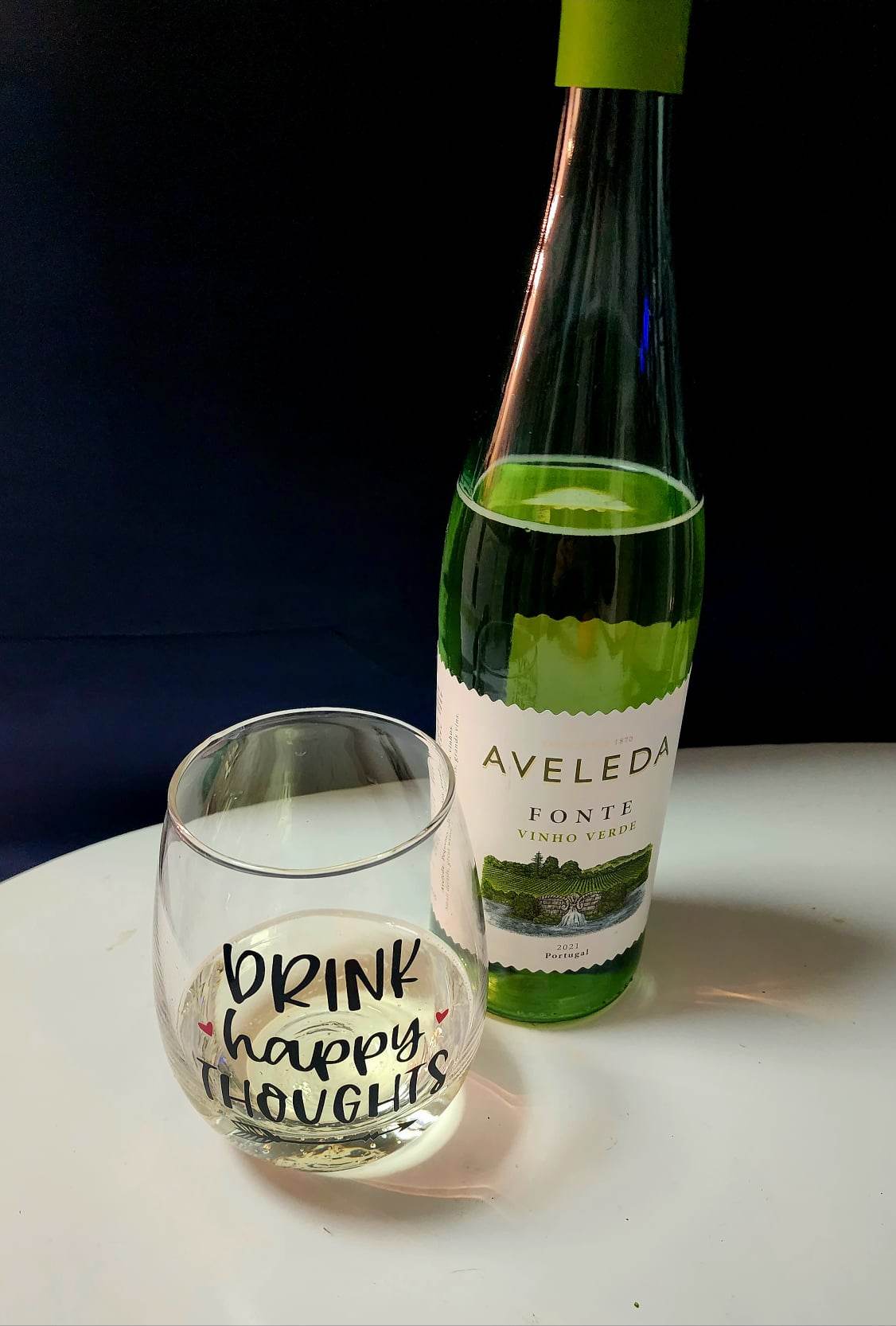 A bottle of Aveleda Vinho Verde and a wine glass that says "drink happy thoughts" 