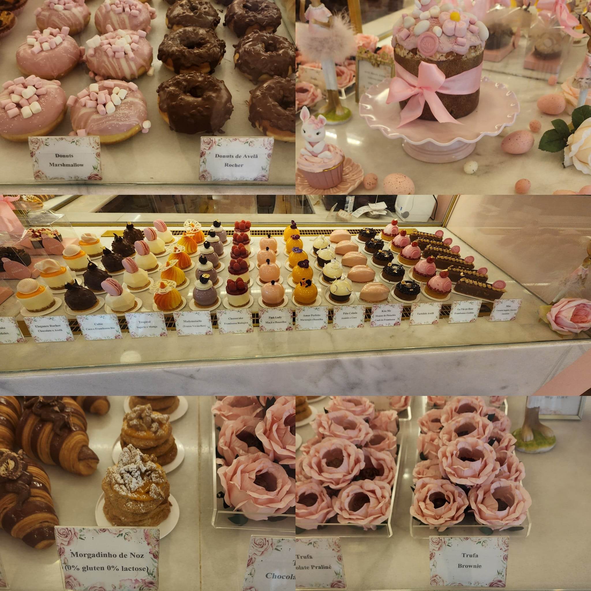 A display of assorted pastries and desserts is showcased, including pink marshmallow and chocolate-covered donuts, elegantly decorated cakes with bows, and a variety of colorful, intricately designed mini cakes and tarts arranged in rows. The setup is on a marble counter, with labels indicating different flavors and dietary options, such as gluten-free and lactose-free. Croissants and flower-shaped truffles add to the visually appealing assortment.