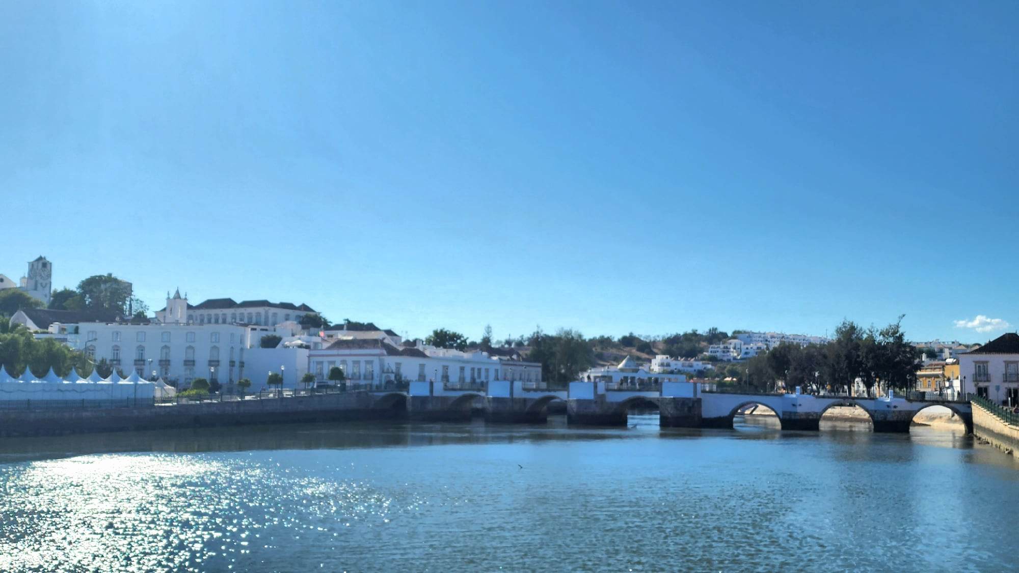 Panoramic view of Tavira Portugal with whitewashed buildings, the Roman bridge and Gilão River reflecting under a clear blue sky