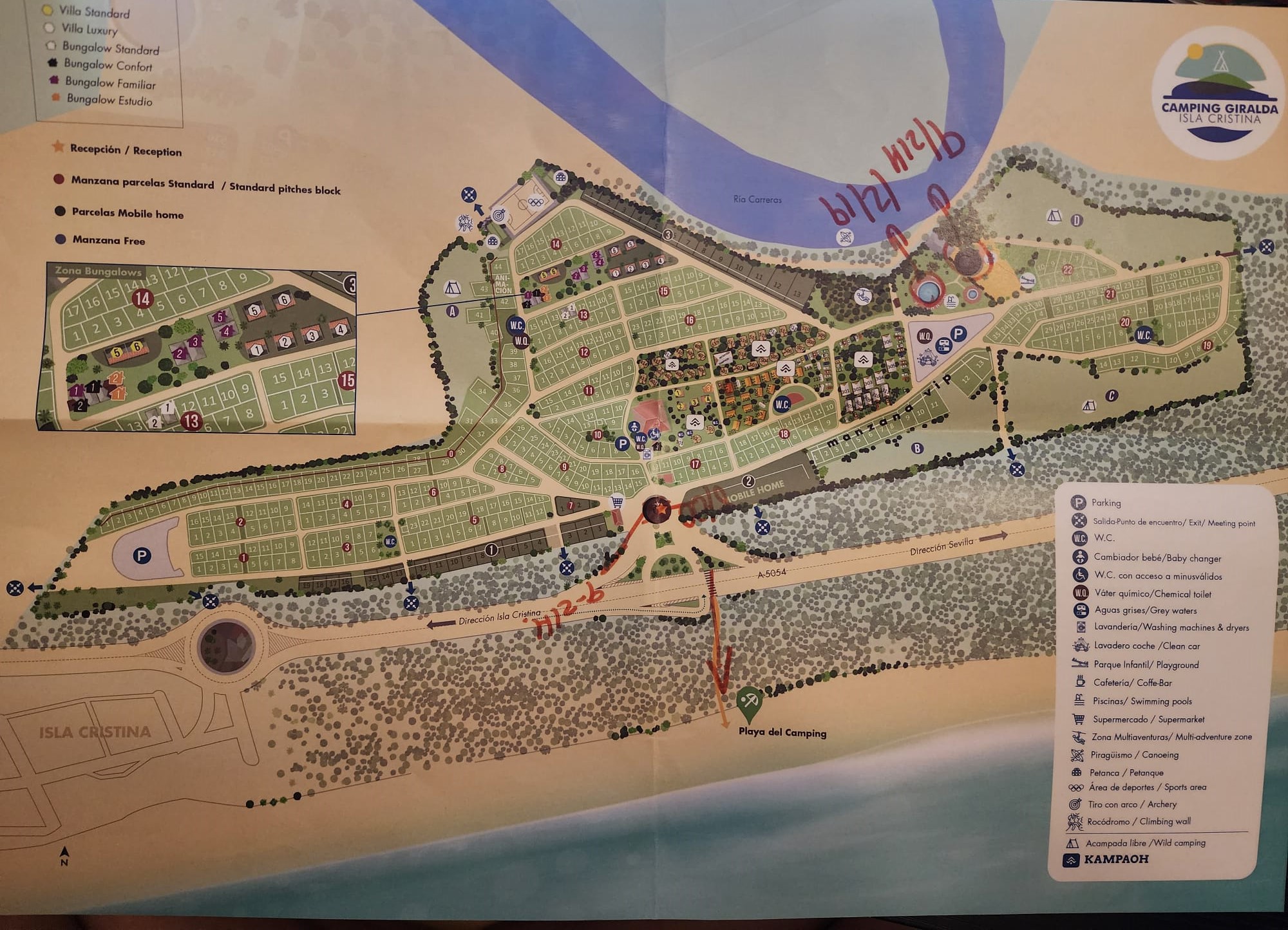 Map of Camping Giralda Isla Cristina, showing various accommodation types like villas and bungalows, pathways, and amenities such as parking, restrooms, and playgrounds. The layout includes areas for standard pitches and mobile homes, with a river and beach nearby. A legend on the right details symbols for facilities like swimming pools and a supermarket.