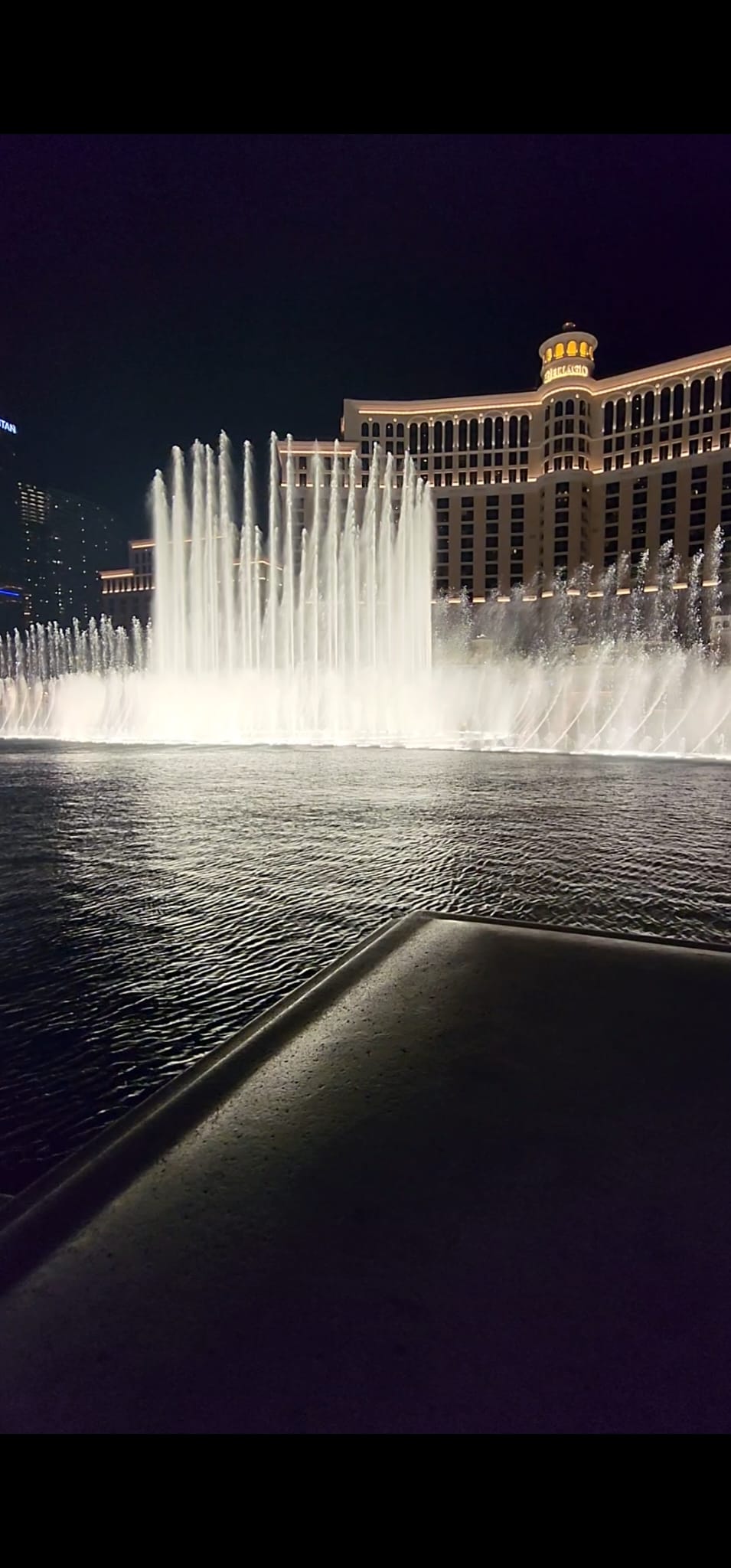 The Bellagio fountain show at night features illuminated jets of water shooting up dramatically against the backdrop of the lit-up Bellagio hotel.