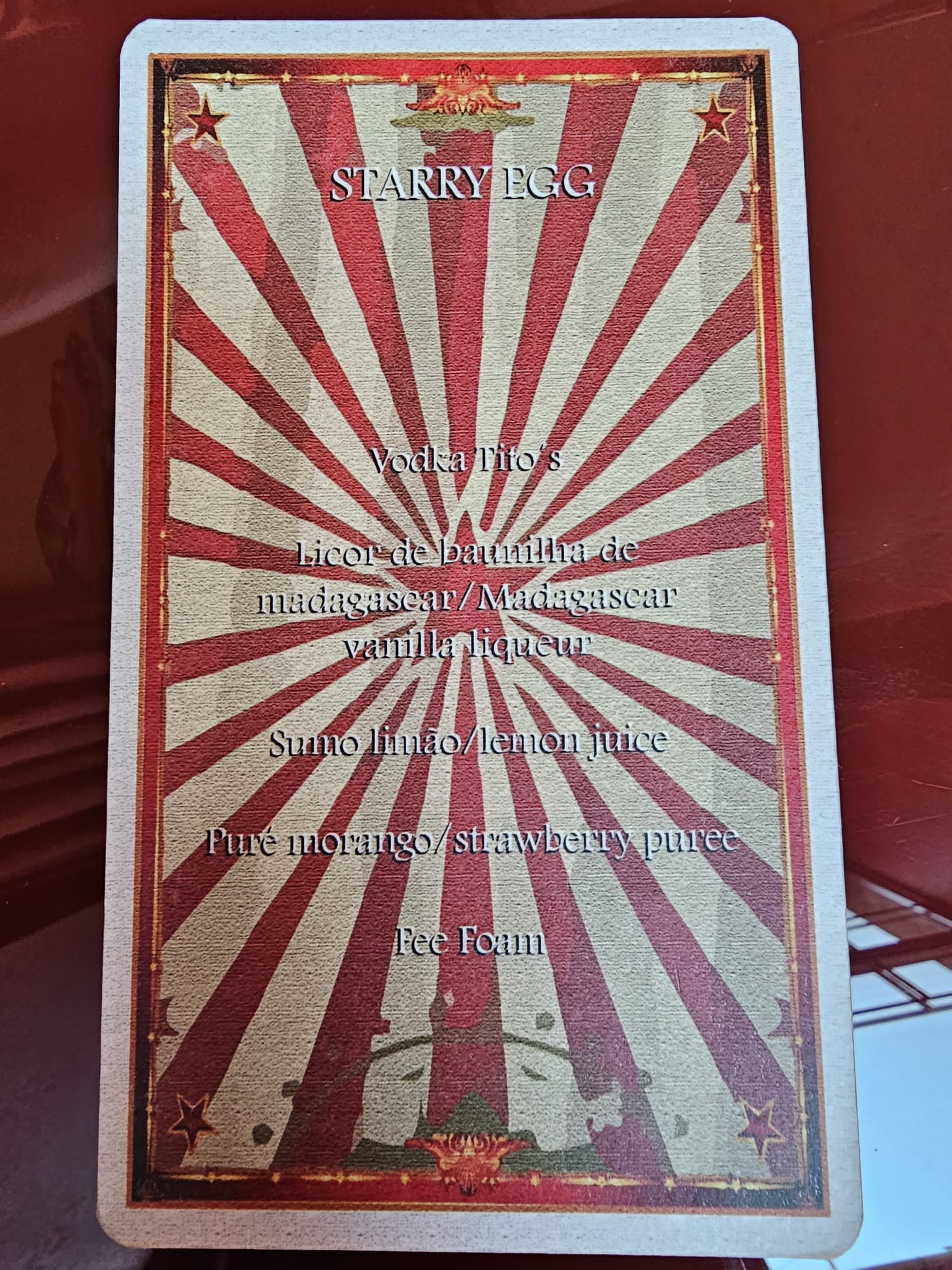 A cocktail menu card titled "Starry Egg" with a red and beige starburst background. It lists ingredients: Tito's Vodka, Madagascar vanilla liqueur, lemon juice, strawberry puree, and egg foam.