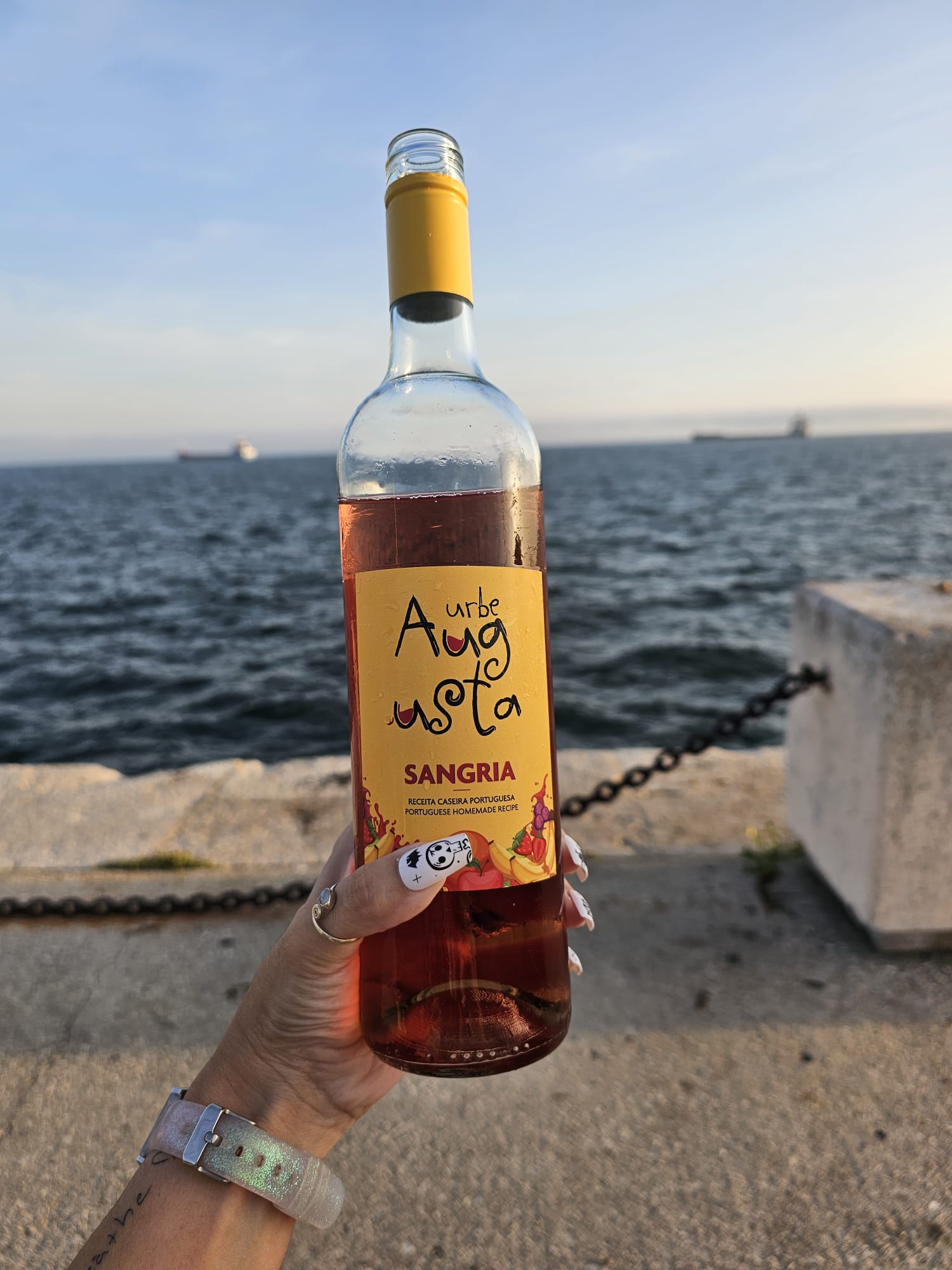 A bottle of sangria held up in front of the ocean in Setubal, Portugal