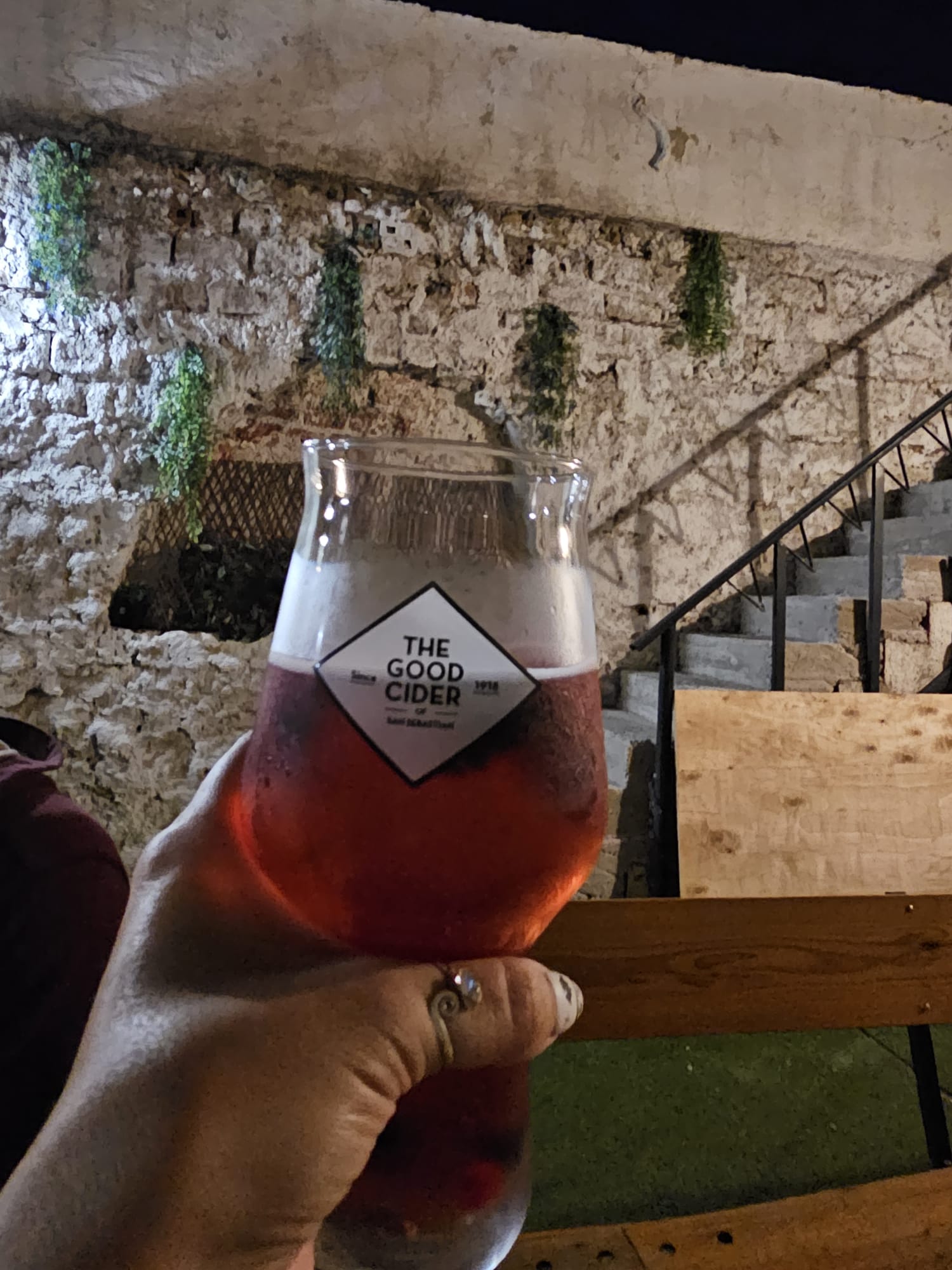 A glass of cider held up in front of a stone wall and staircase