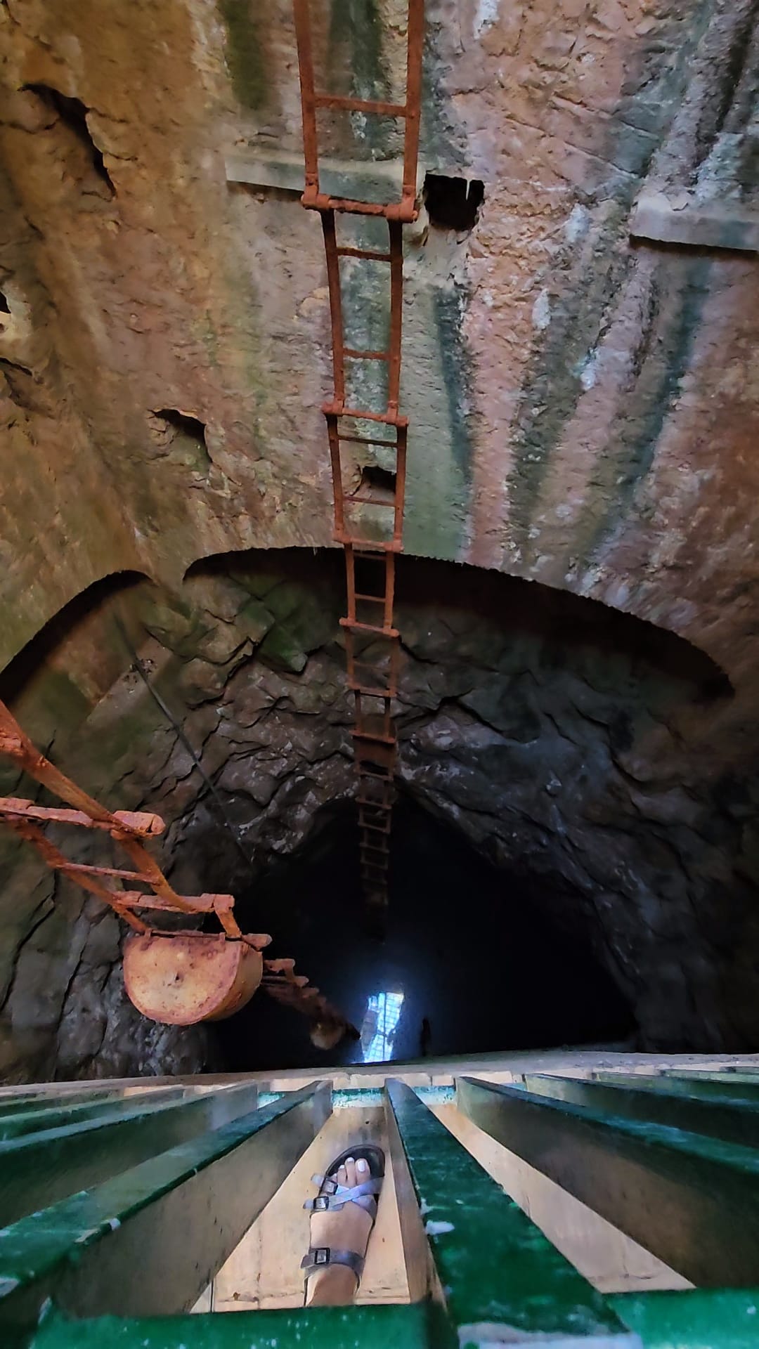 View looking down into a deep stone well with a clay water jug and iron ladder at a Portuguese museum