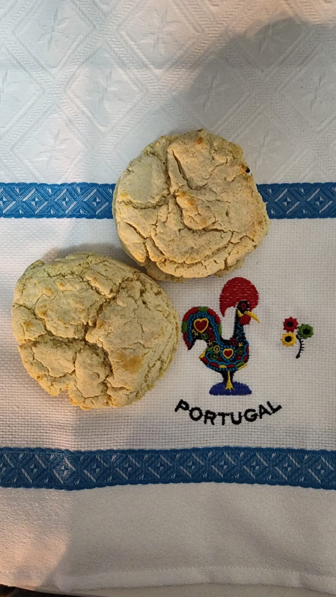 Two homemade gluten-free biscuits resting on a Portuguese tea towel featuring the iconic Galo de Barcelos rooster