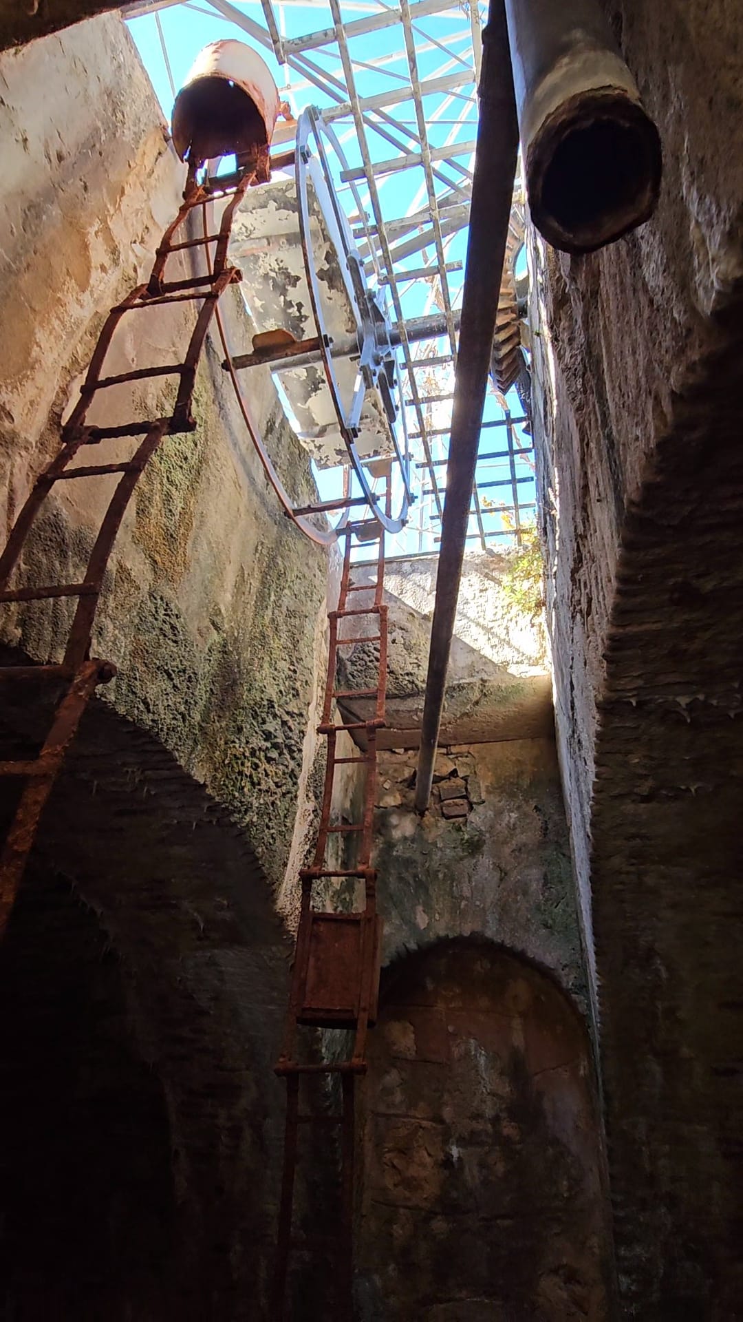 View looking up from inside an ancient stone well showing the iron ladder rungs and blue sky above at a heritage museum in Portugal