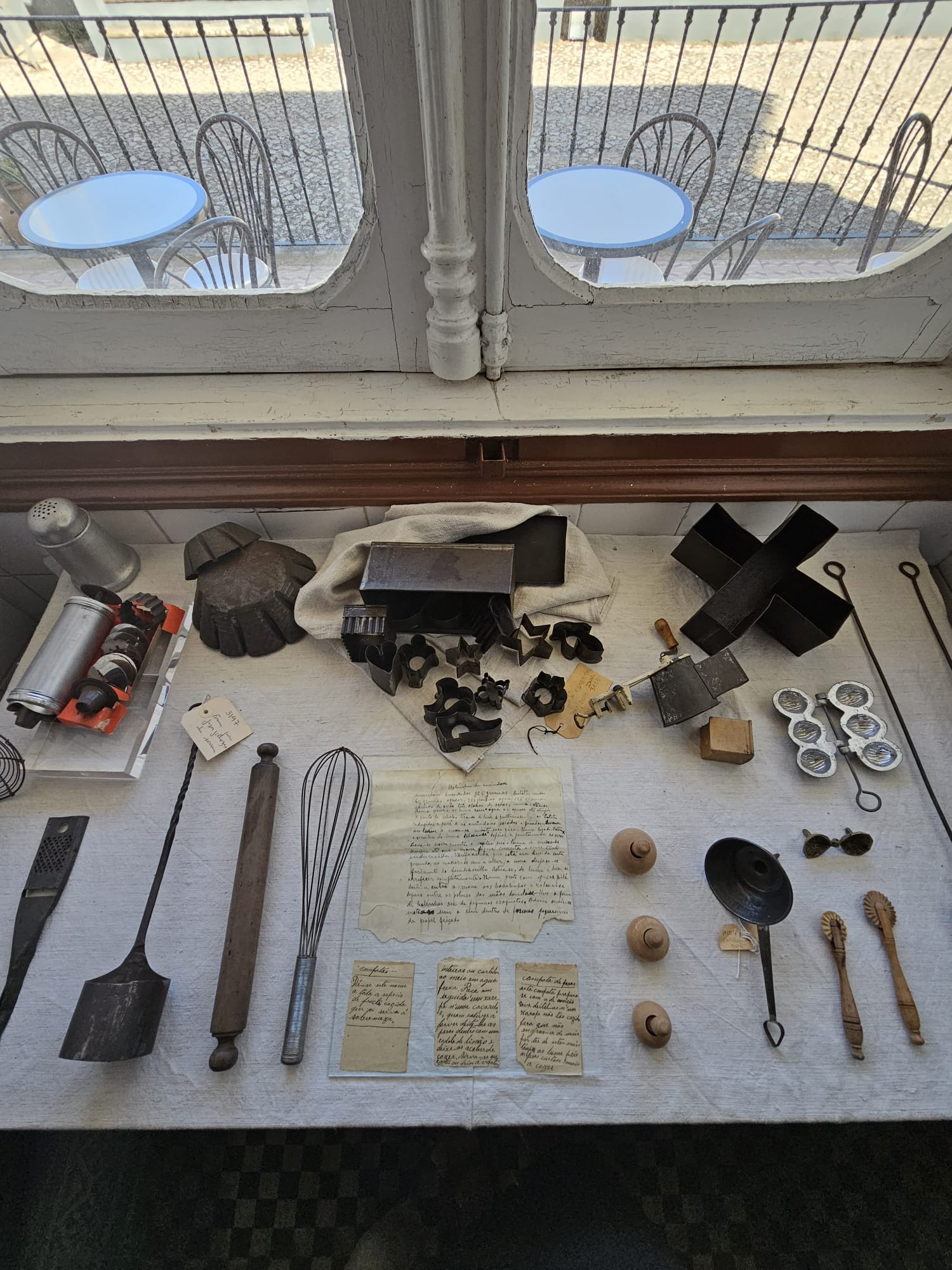 Collection of antique baking tools including cookie cutters, rolling pin, whisk, molds and handwritten recipes displayed on a table at a Portuguese heritage museum