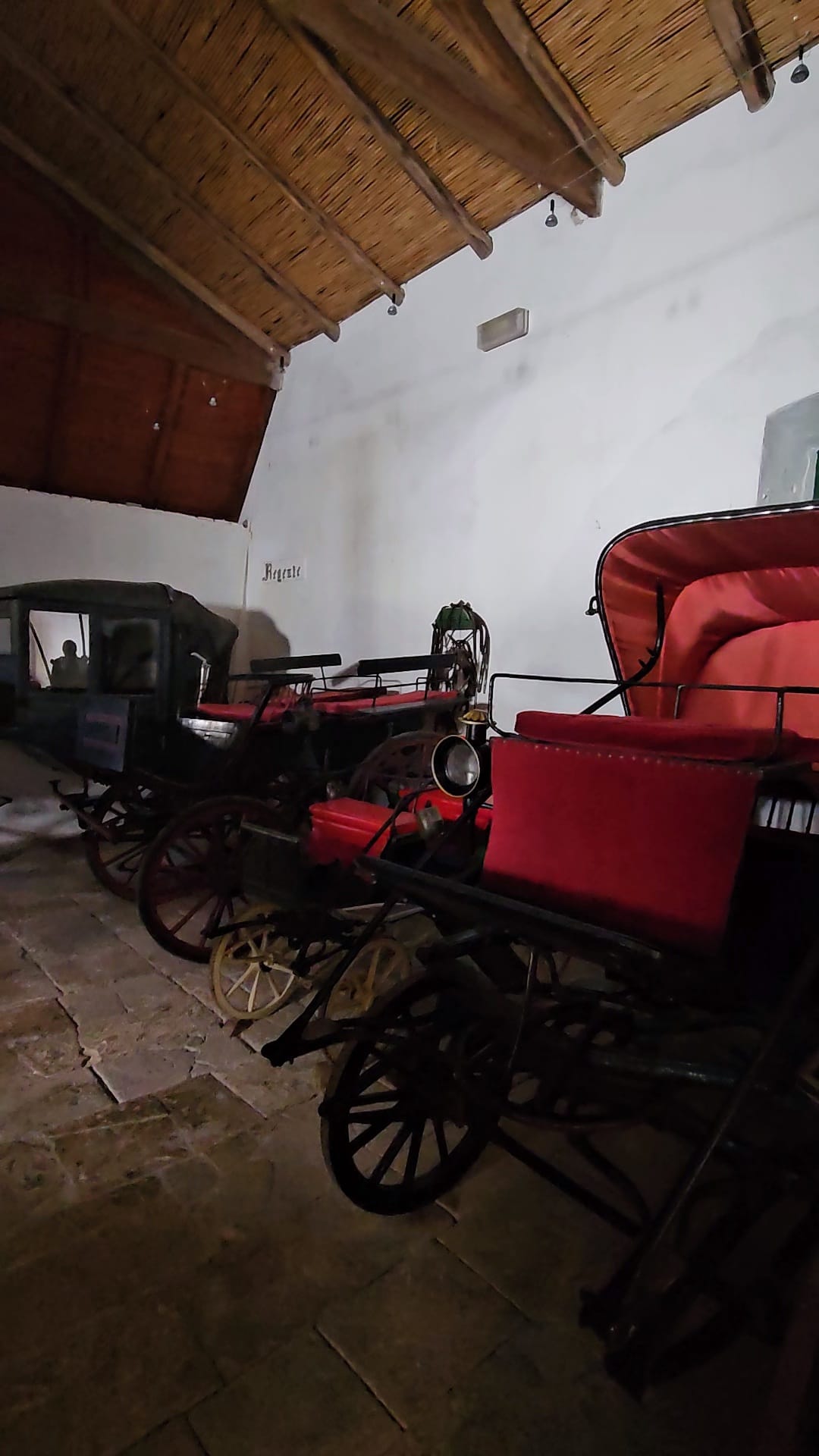 Collection of restored antique horse drawn carriages with red velvet upholstery inside a Portuguese heritage museum