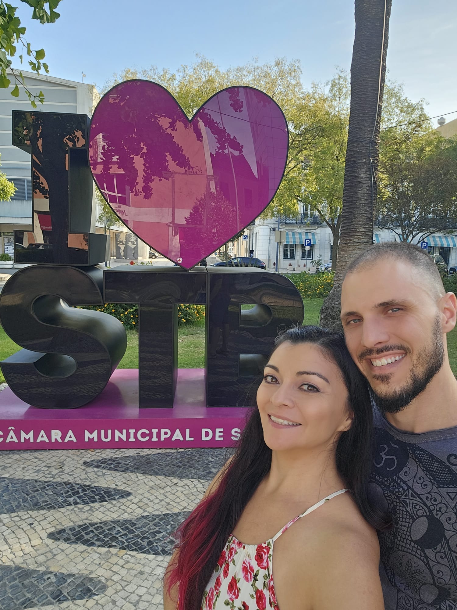 A smiling couple posed in front of the I ❤️STB sign in Setubal, Portugal