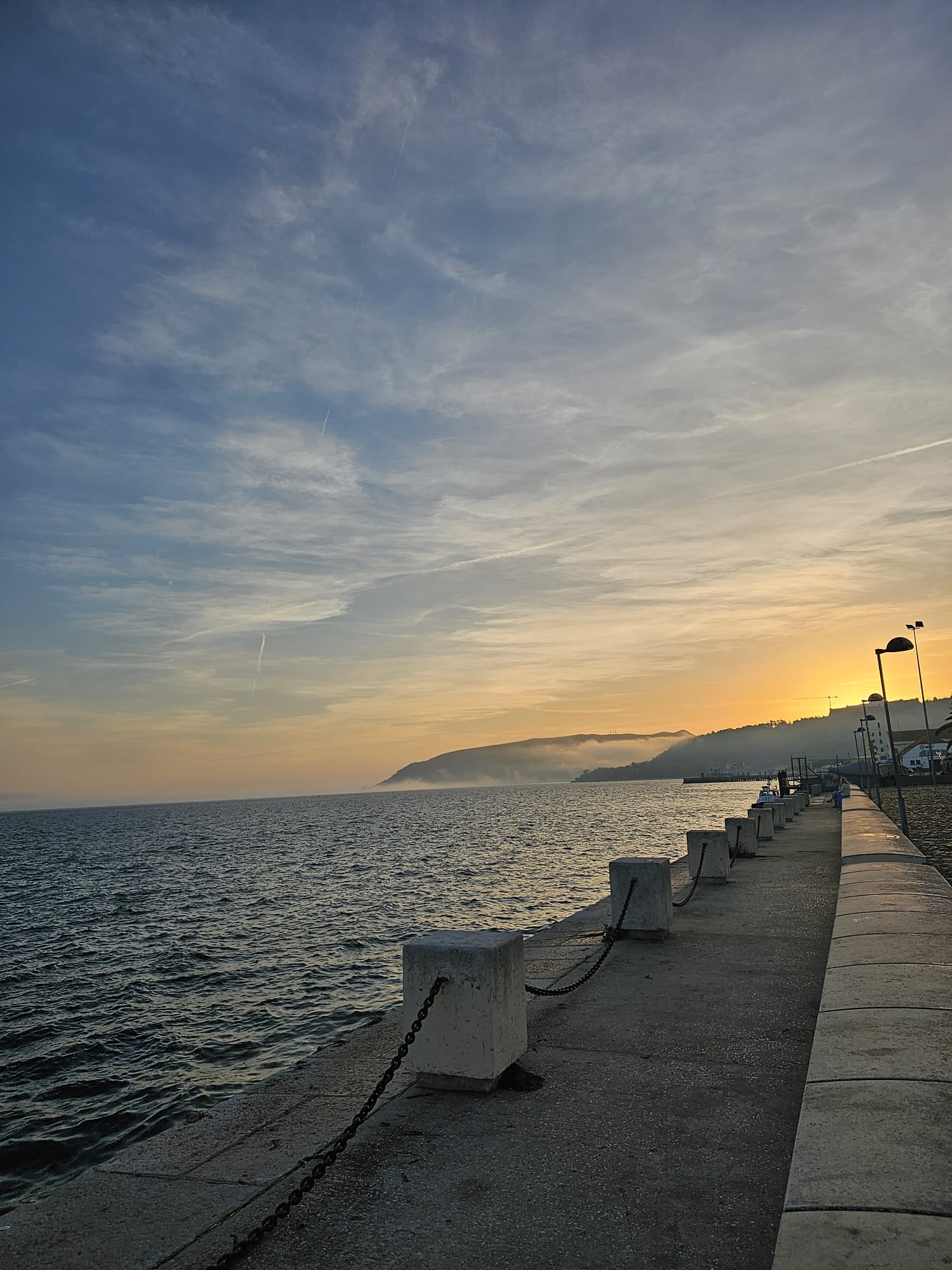 Waterfront walkway at sunset with a mountain in the background