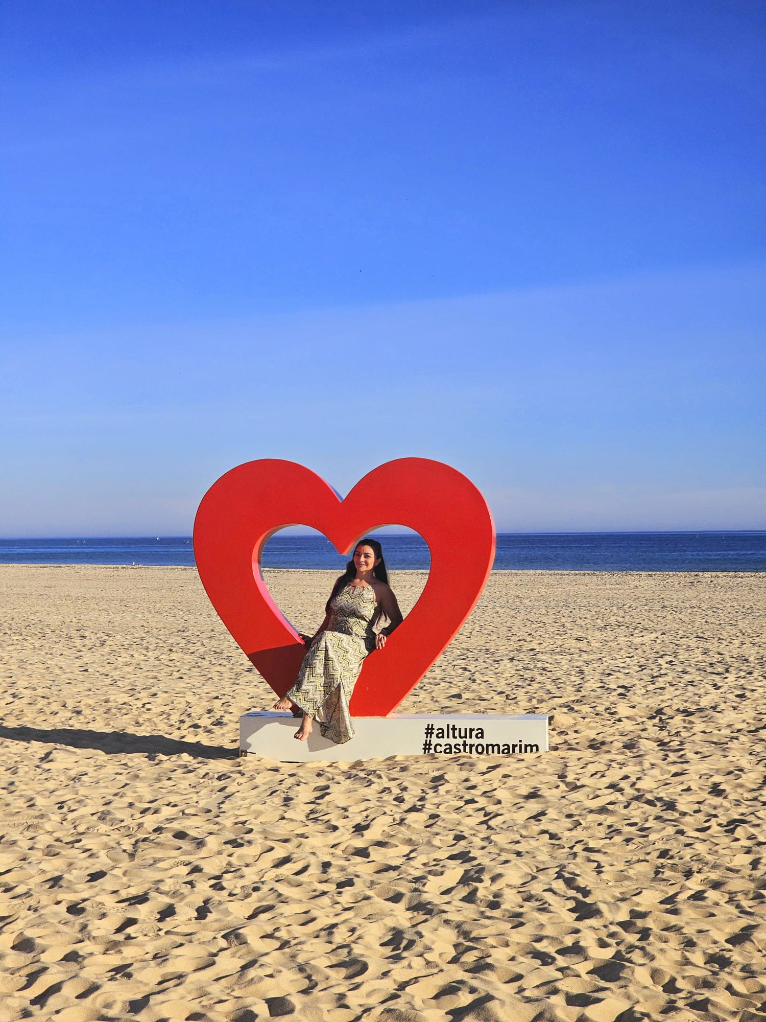 Woman posing inside a large red heart shaped photo installation on Altura beach in the Eastern Algarve Portugal