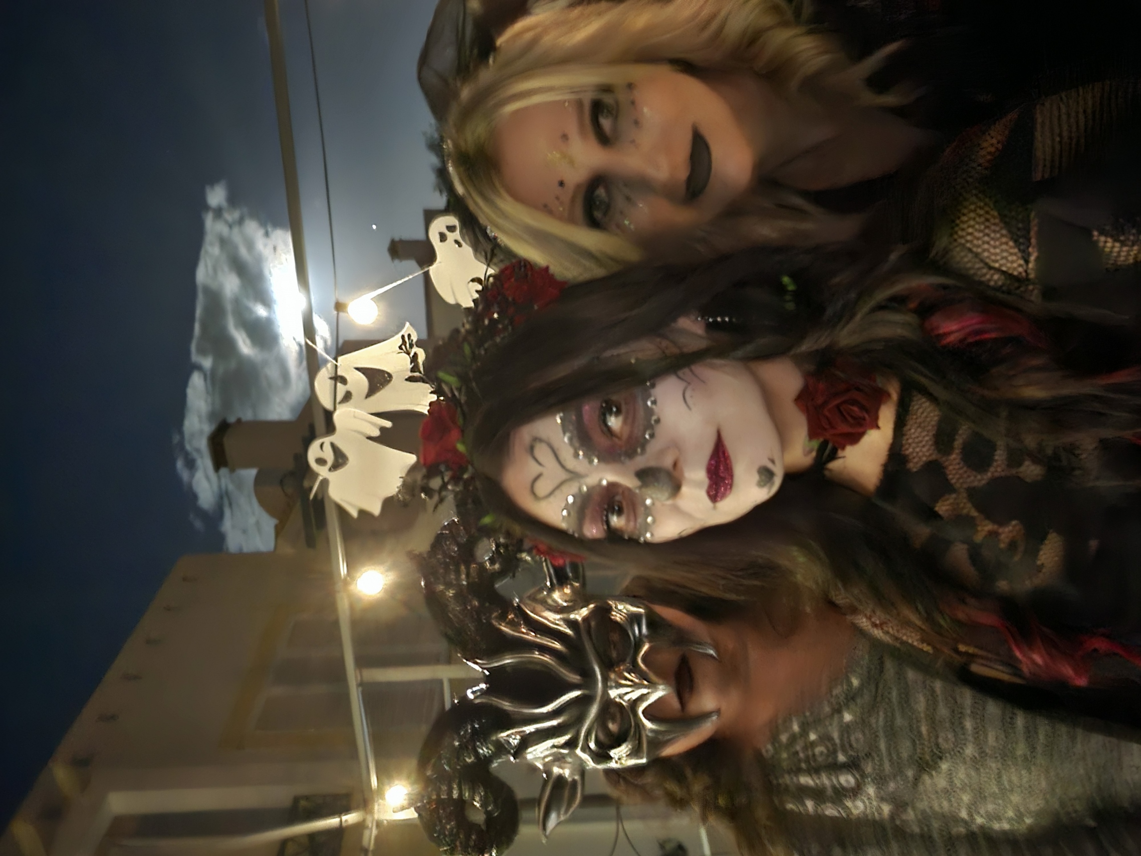 Friends in Halloween costumes including sugar skull and masquerade mask makeup at an outdoor Halloween