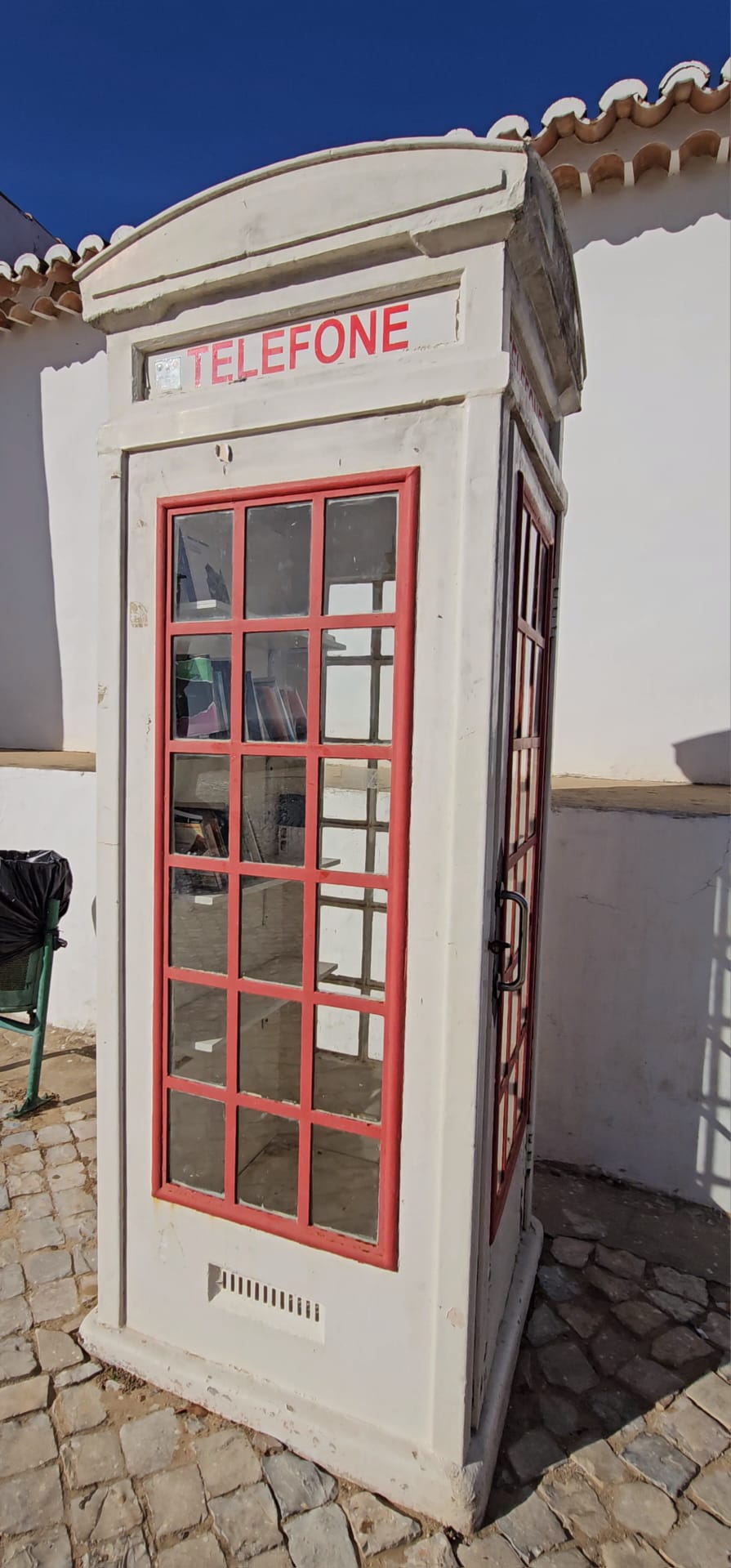 Vintage white and red Portuguese telephone booth outside whitewashed buildings in Cacela Velha Portugal