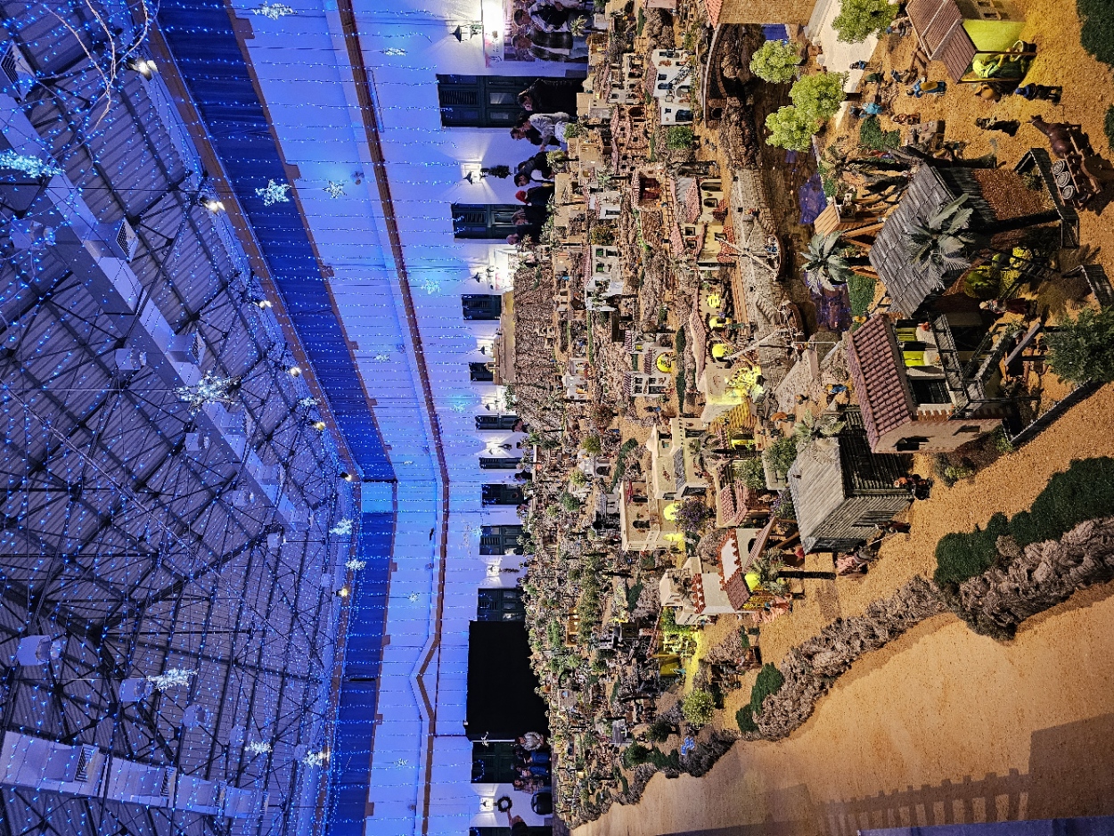 Full panoramic view of the enormous nativity scene filling the entire exhibition hall under blue star lights