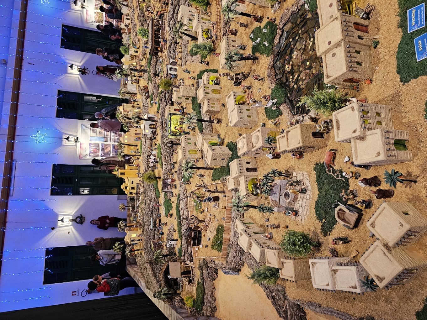 Ground level view of visitors admiring the massive nativity scene display under blue lights