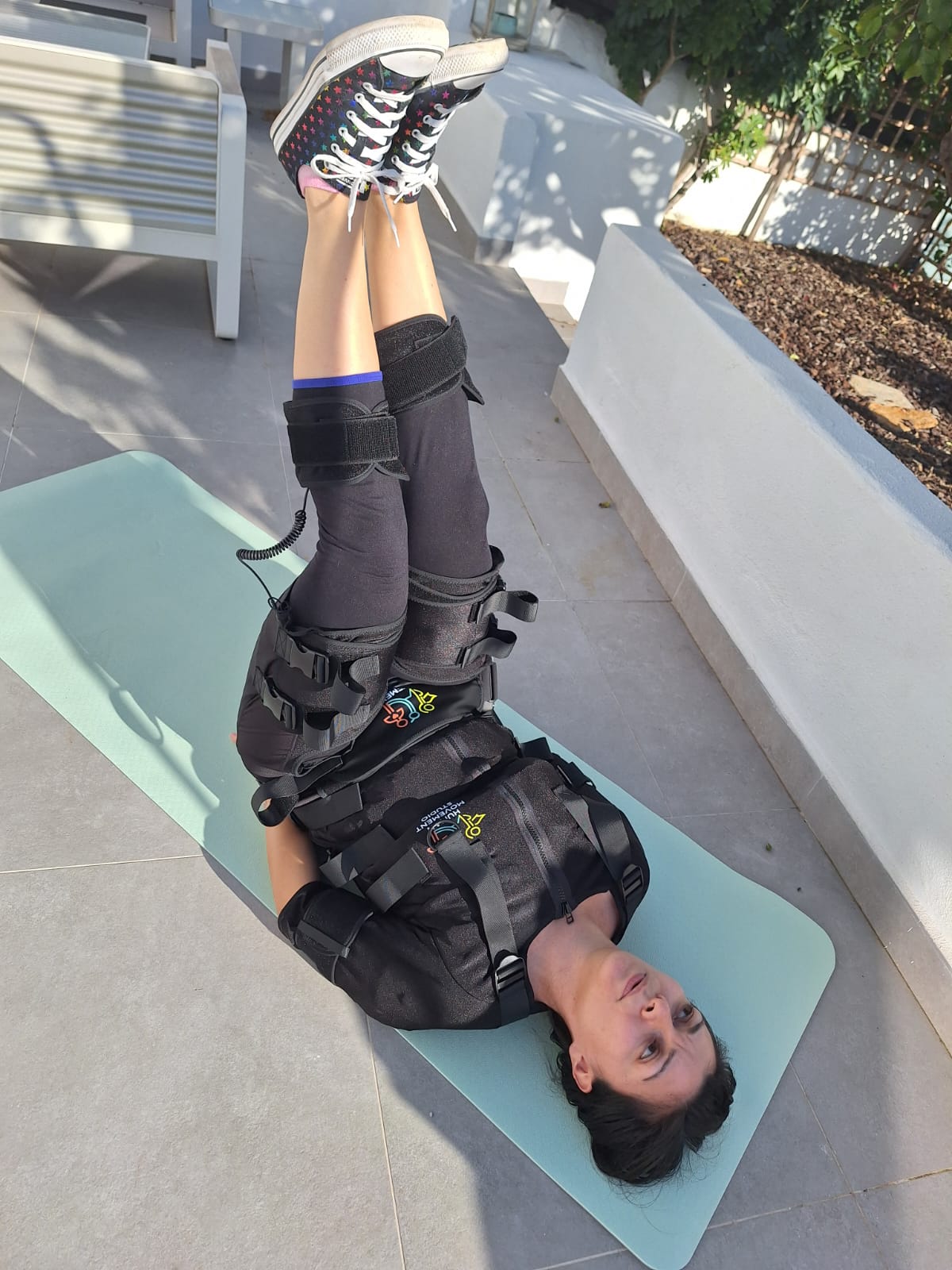 Woman lying on a yoga mat in an EMS training suit with legs raised in the air during an EMS workout session at Human Movement Studio Portugal