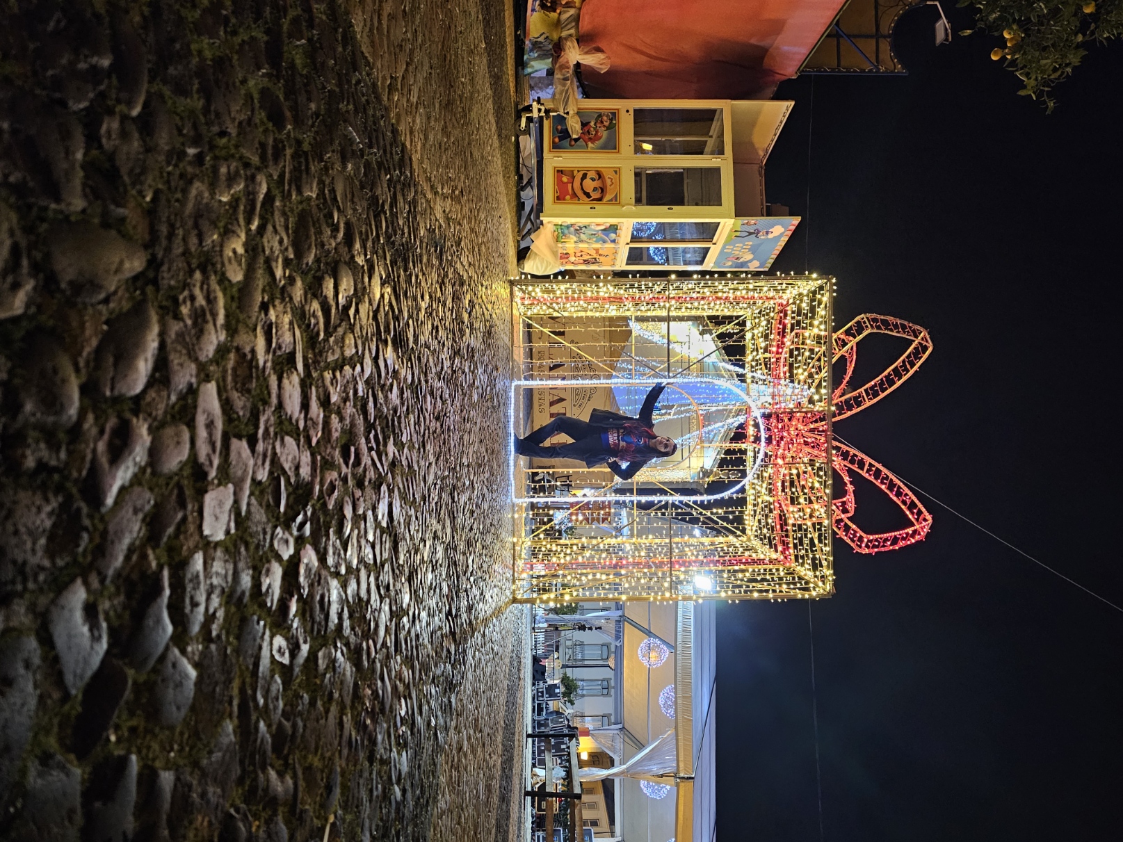 Woman posing inside a giant illuminated Christmas gift light installation photo spot at the VRSA Christmas Village Portugal
