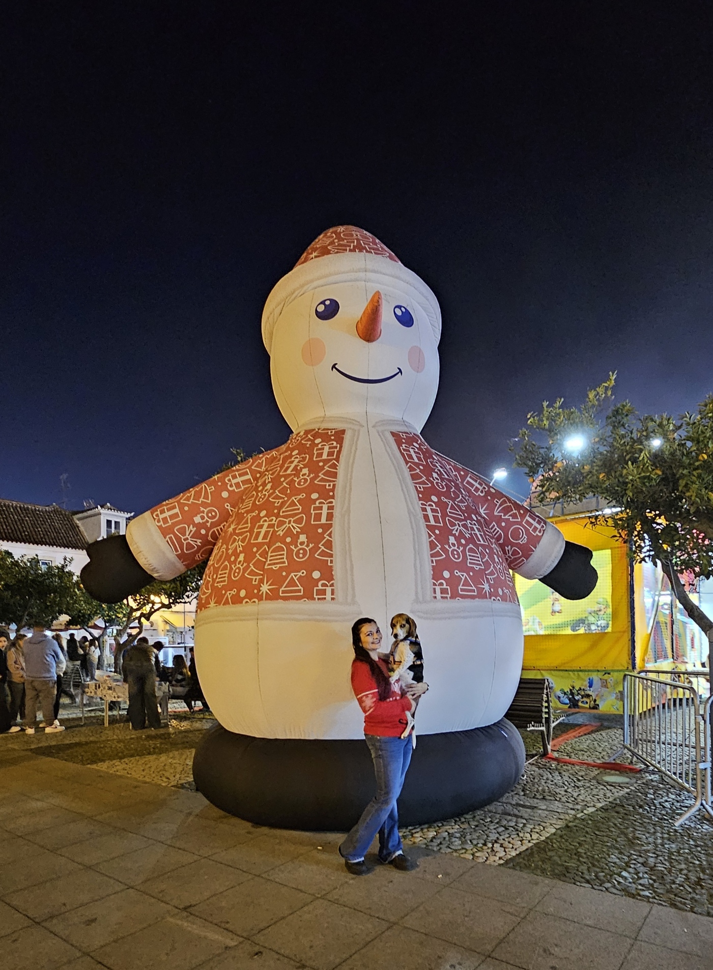 Woman holding a beagle dog in front of a giant inflatable snowman decoration at the VRSA Christmas Village in Portugal