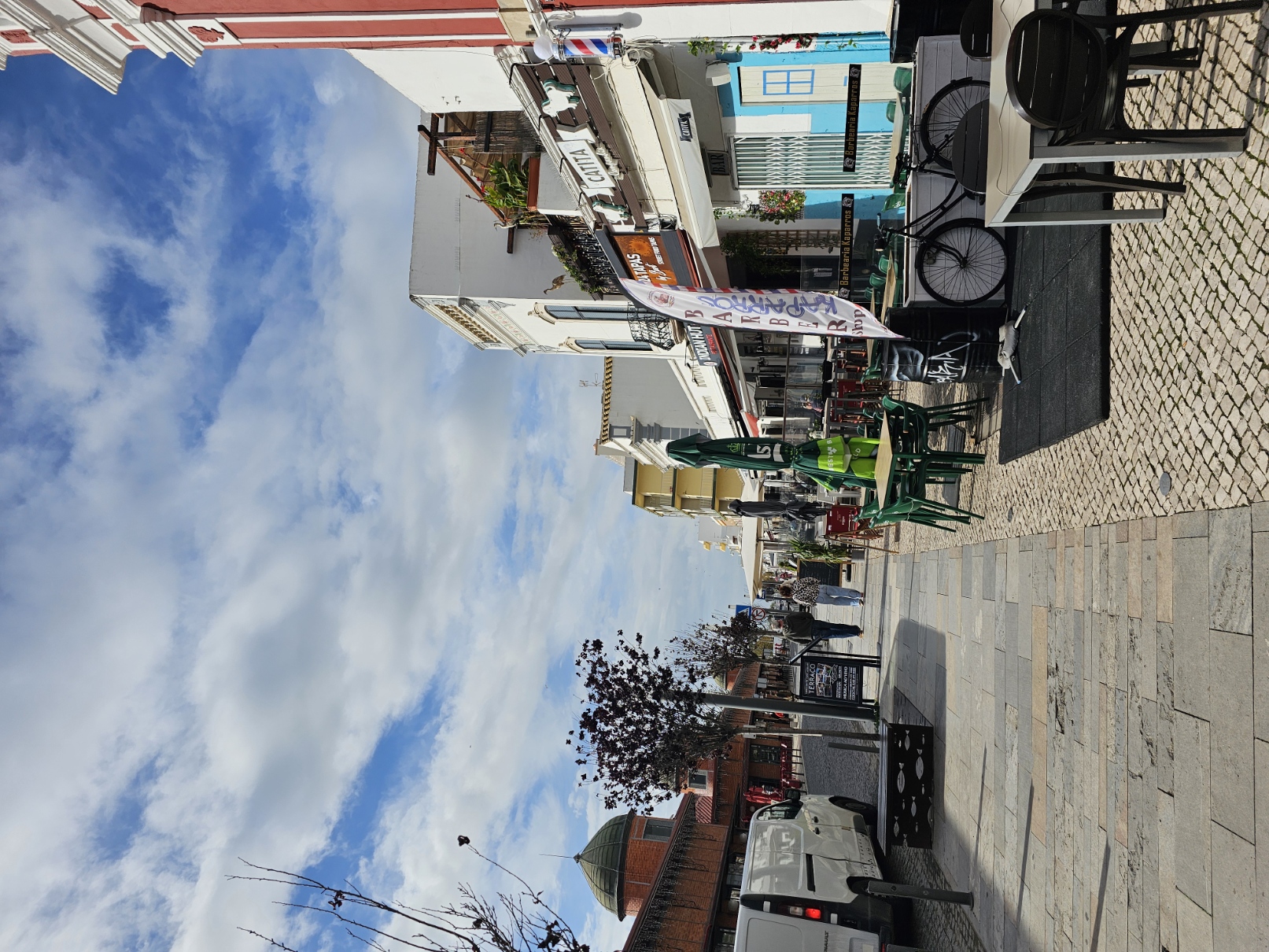 Pedestrian street Avenida 5 de Outubro in Olhão Portugal lined with outdoor cafe seating and colorful shopfronts under a blue sky