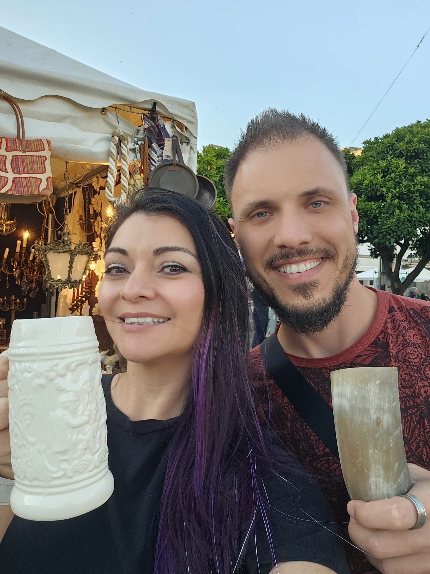 Couple smiling and holding decorative ceramic steins at a historical festival market in Portugal
