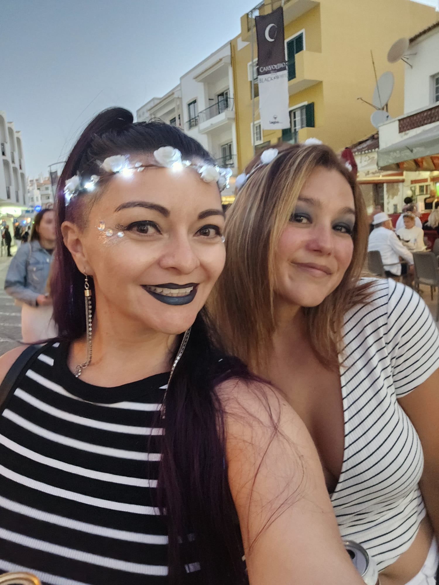 Two women in matching black and white striped outfits smiling at the Carvoeiro Black and White Night festival in the Algarve, Portugal