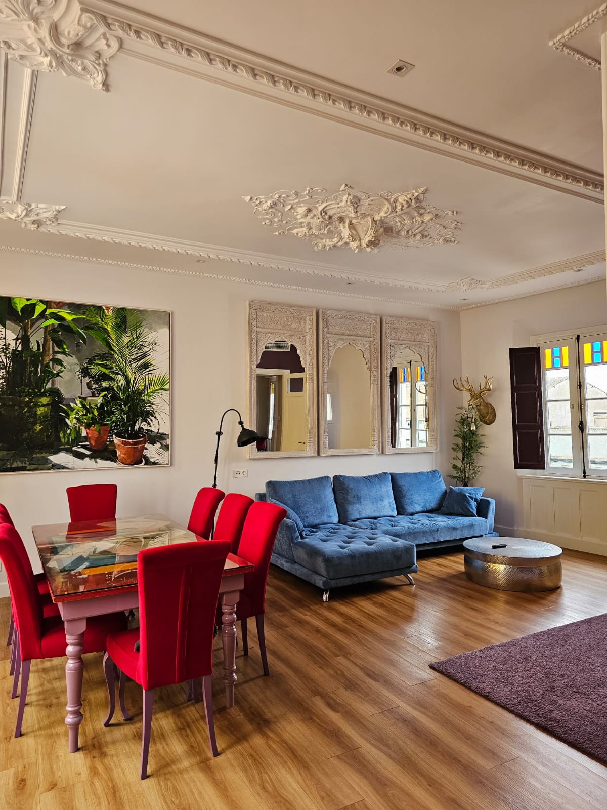 Elegant living room with ornate plaster ceiling moldings, blue velvet sofa and red chairs at Casa Verde apartments