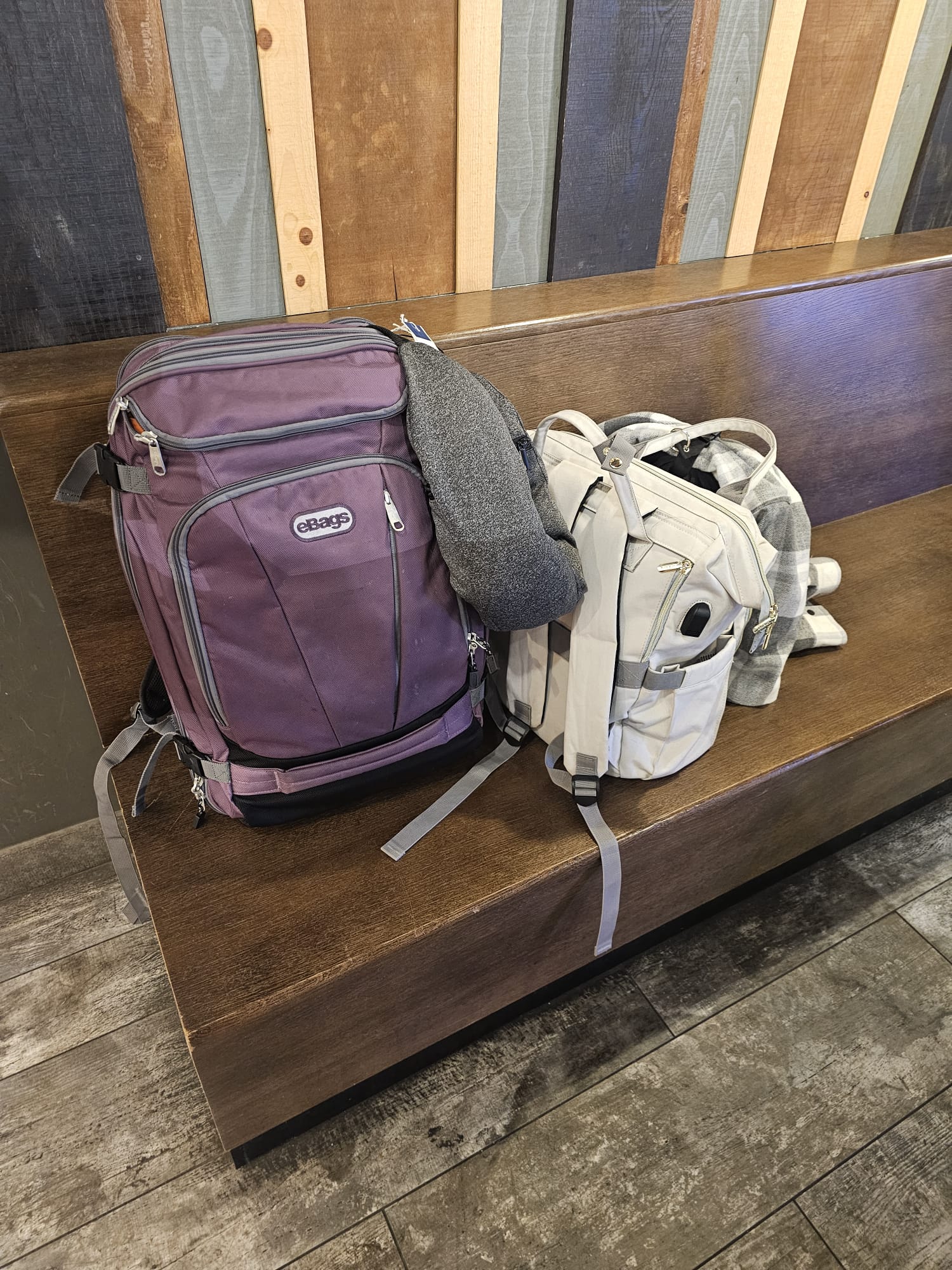 Two carry-on backpacks sitting on a wooden bench at Amsterdam Schiphol Airport, packed for a two-week trip to the US