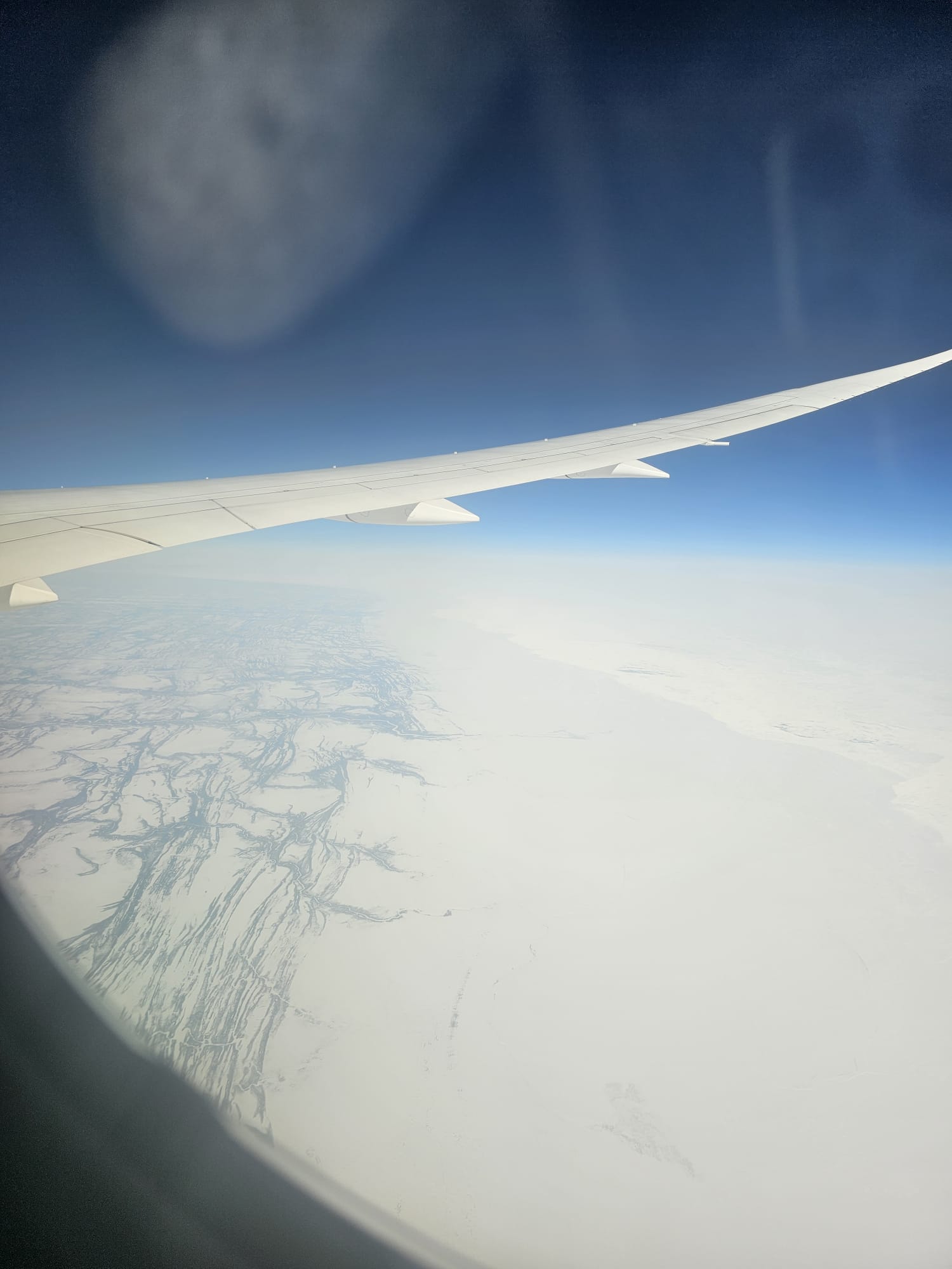Aerial view of Greenland's icy terrain and frozen river patterns seen from an airplane window during a transatlantic flight