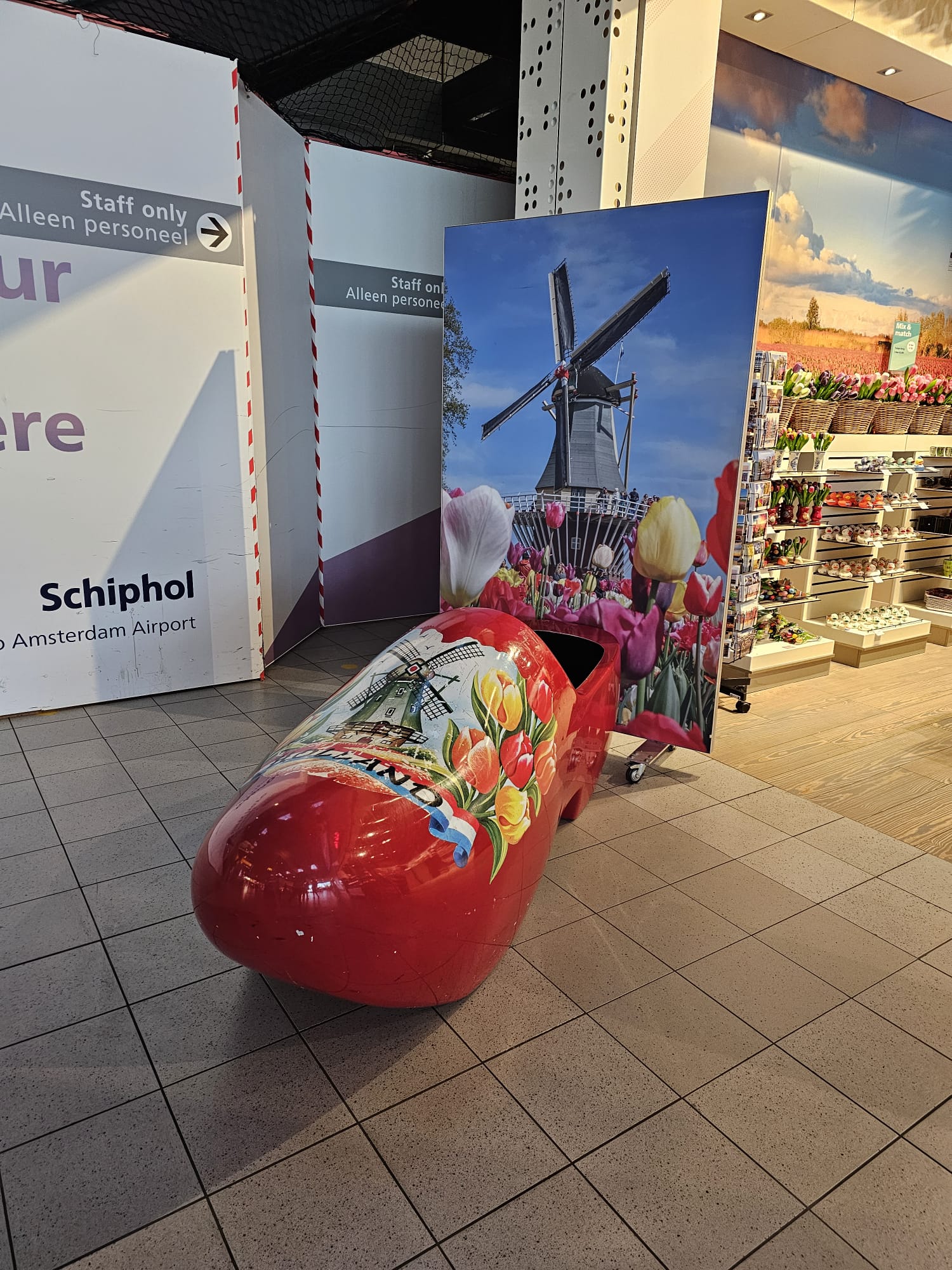 Giant red Dutch wooden clog souvenir display at Amsterdam Schiphol Airport with windmill imagery in the background