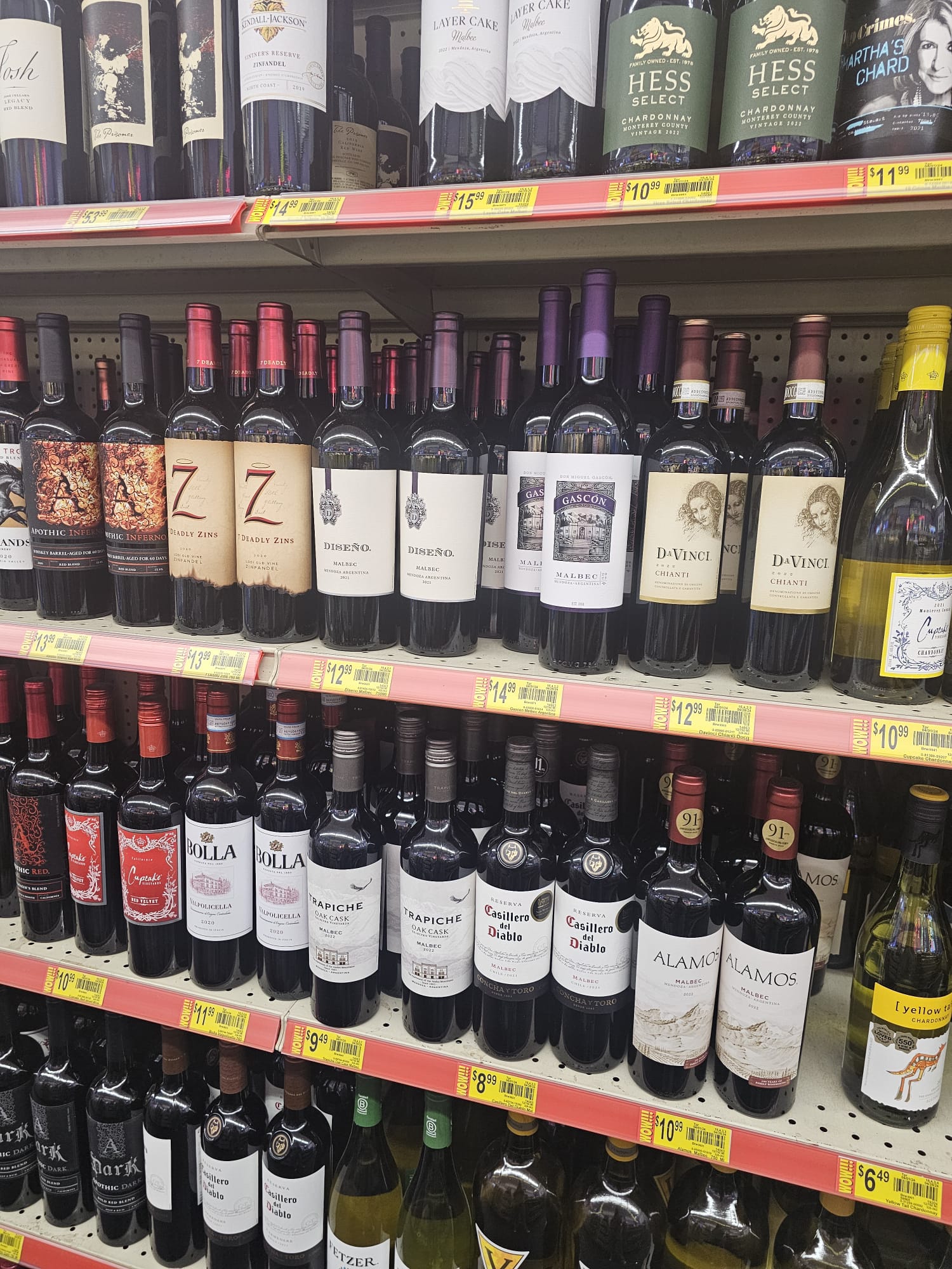 Multiple shelves of wine bottles with price tags at an American grocery store, featuring brands like Casillero del Diablo, Alamos, and DaVinci Chianti