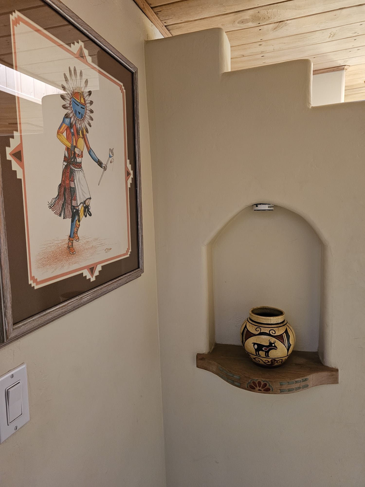 Framed Kachina figure painting and traditional Native American clay pot displayed in an adobe wall niche at Casas de Suenos in Albuquerque