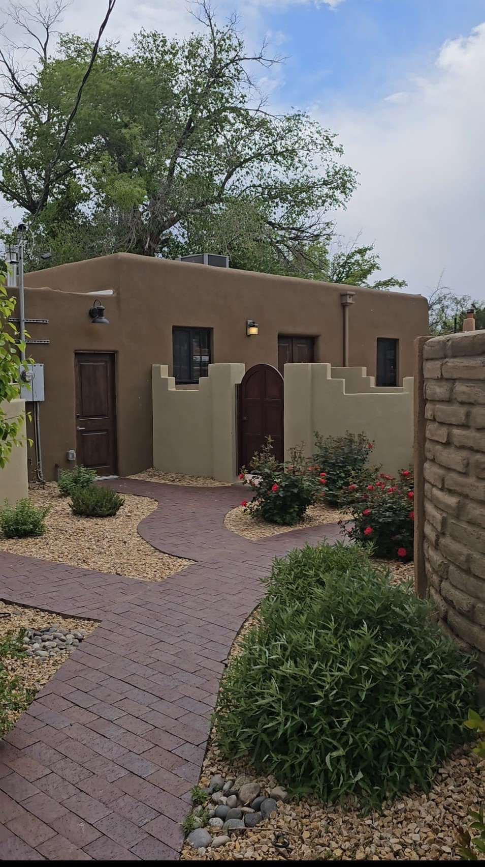 Charming adobe casita exterior with desert landscaping, red roses, and a brick pathway at Casas de Suenos in Albuquerque