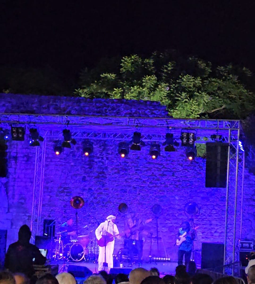 Live concert performance on a dramatically lit purple stage set against ancient castle walls at the Mediterranean Diet Fair in Tavira, Portugal