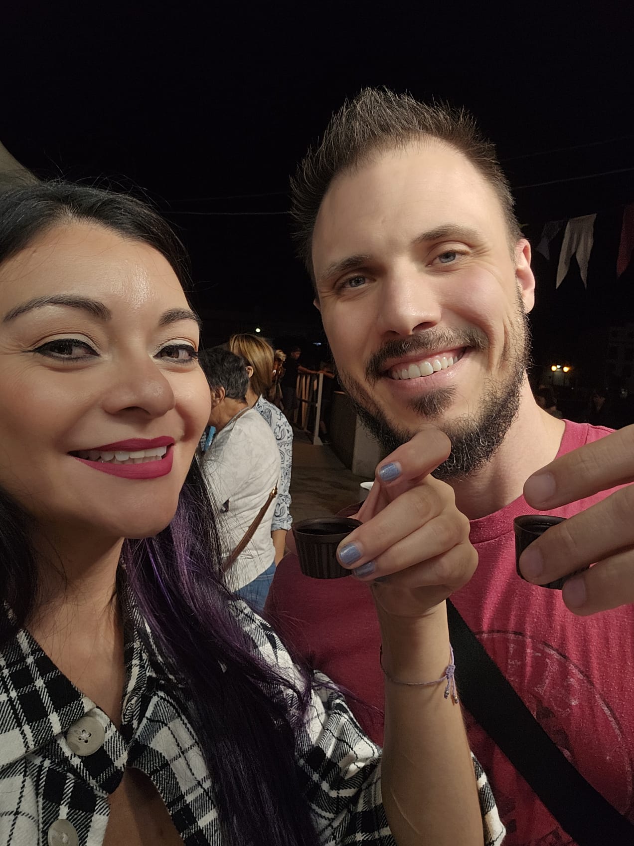 Couple smiling and holding ginja shots at an outdoor evening festival in Portugal