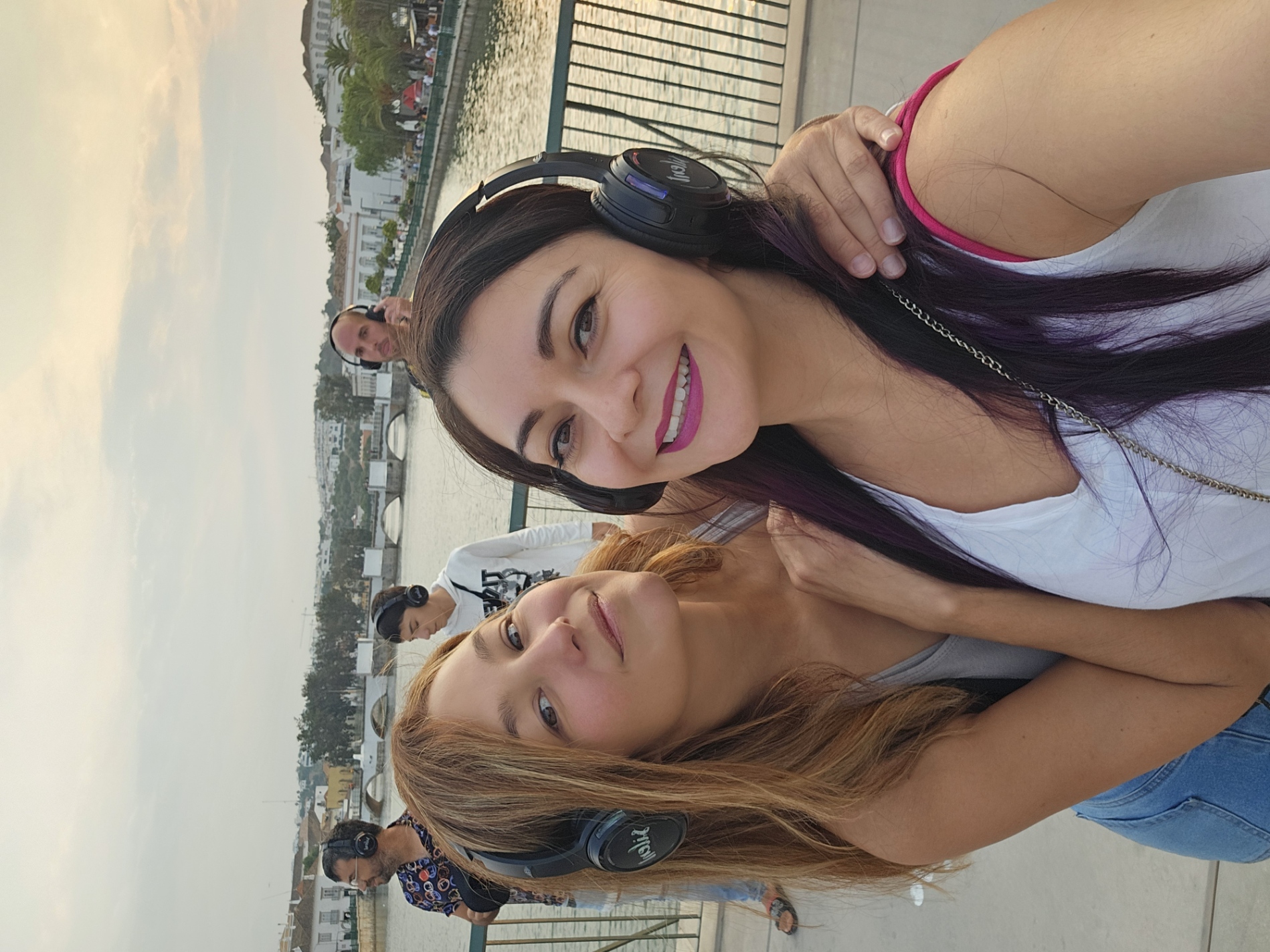 two women wearing wireless headphones at a silent disco party on a bridge overlooking the Gilao River in Tavira, Portugal, during Festa da Juventude