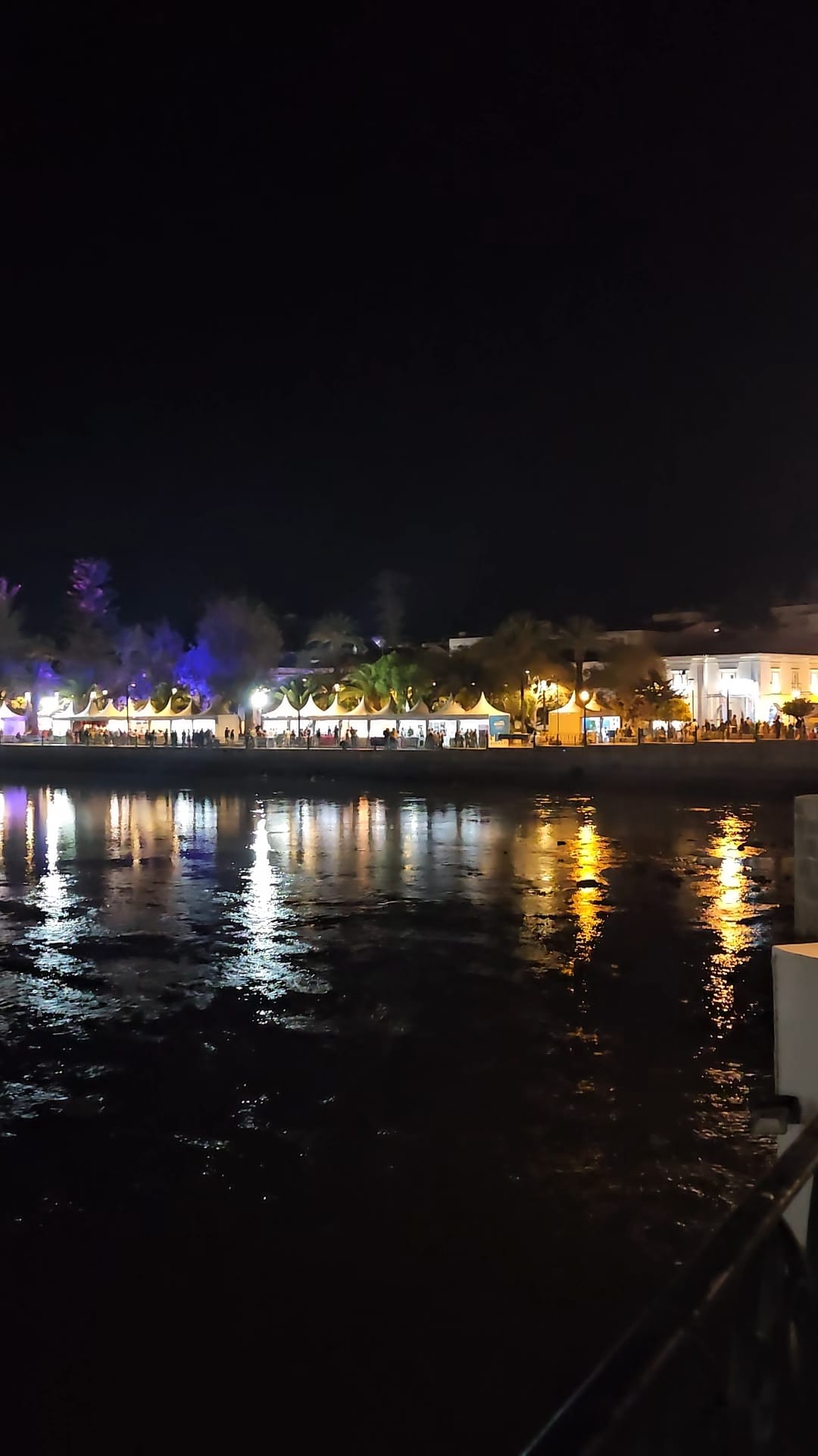 Colorful festival lights reflecting on the water at a lively Mediterranean Diet Fair in Tavira, Portugal at night