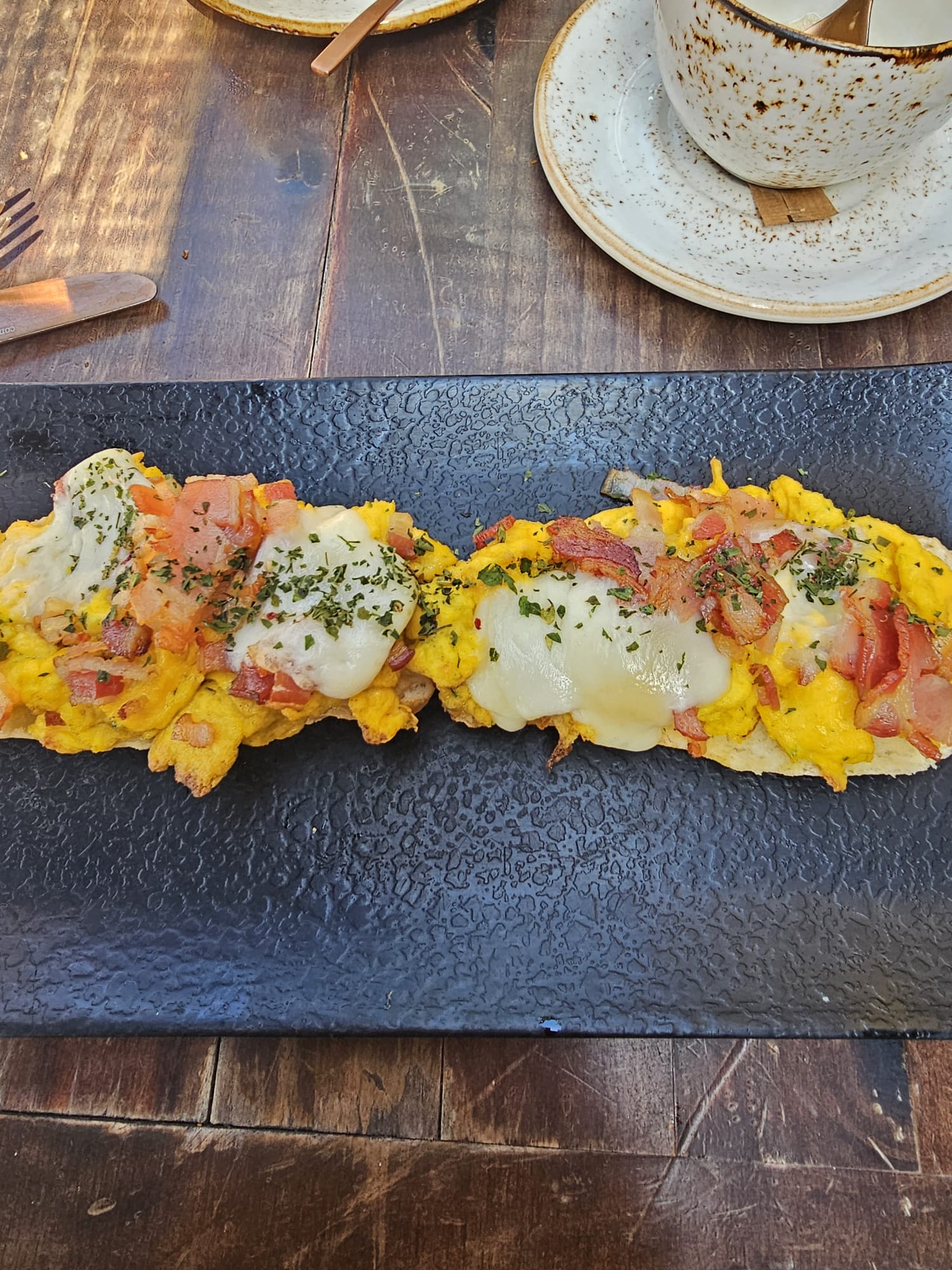 a close-up of gluten-free toast topped with scrambled eggs, bacon, and melted cheese.