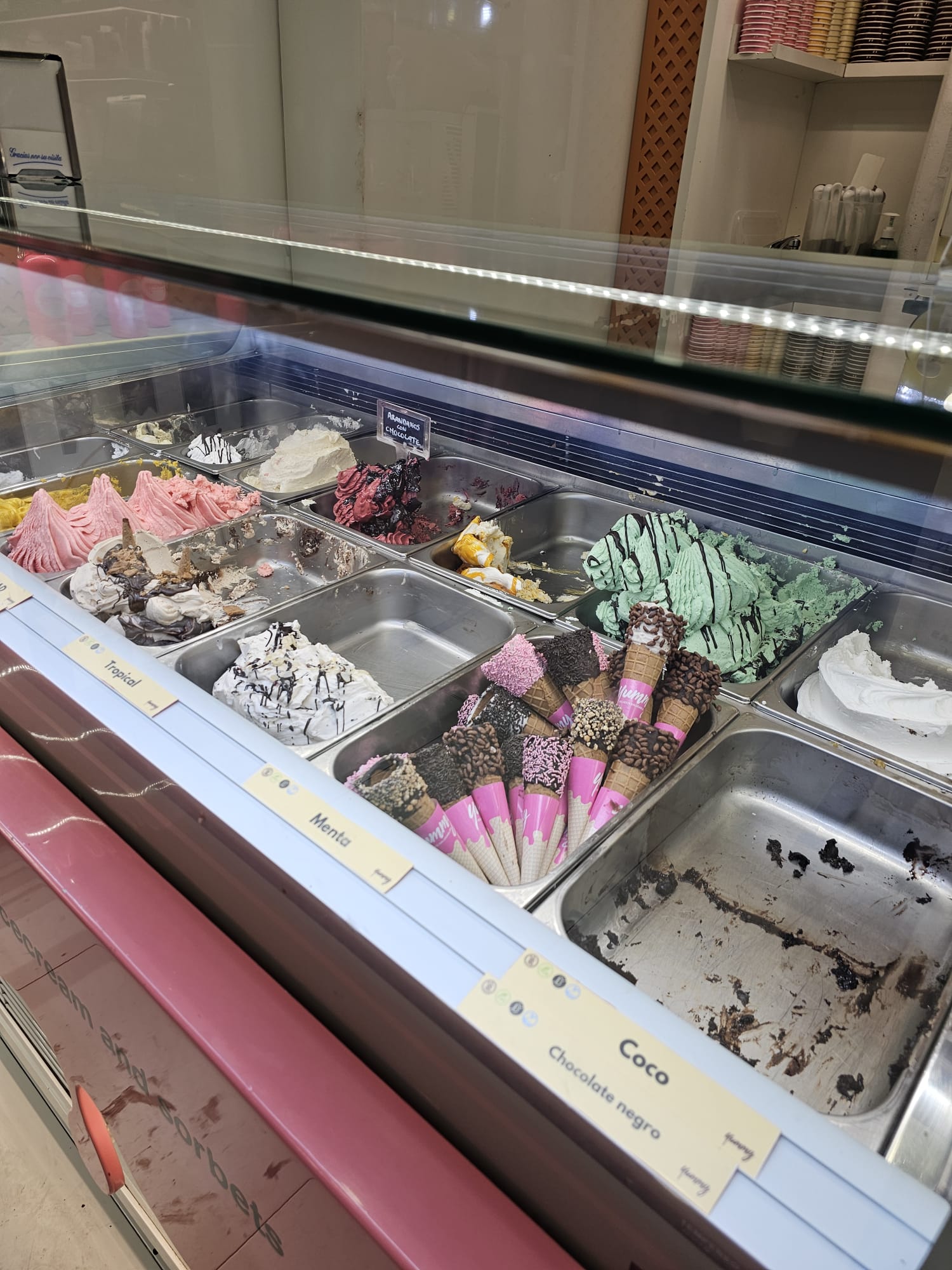 An ice cream case with assorted flavors and chocolate dipped ice cream cones