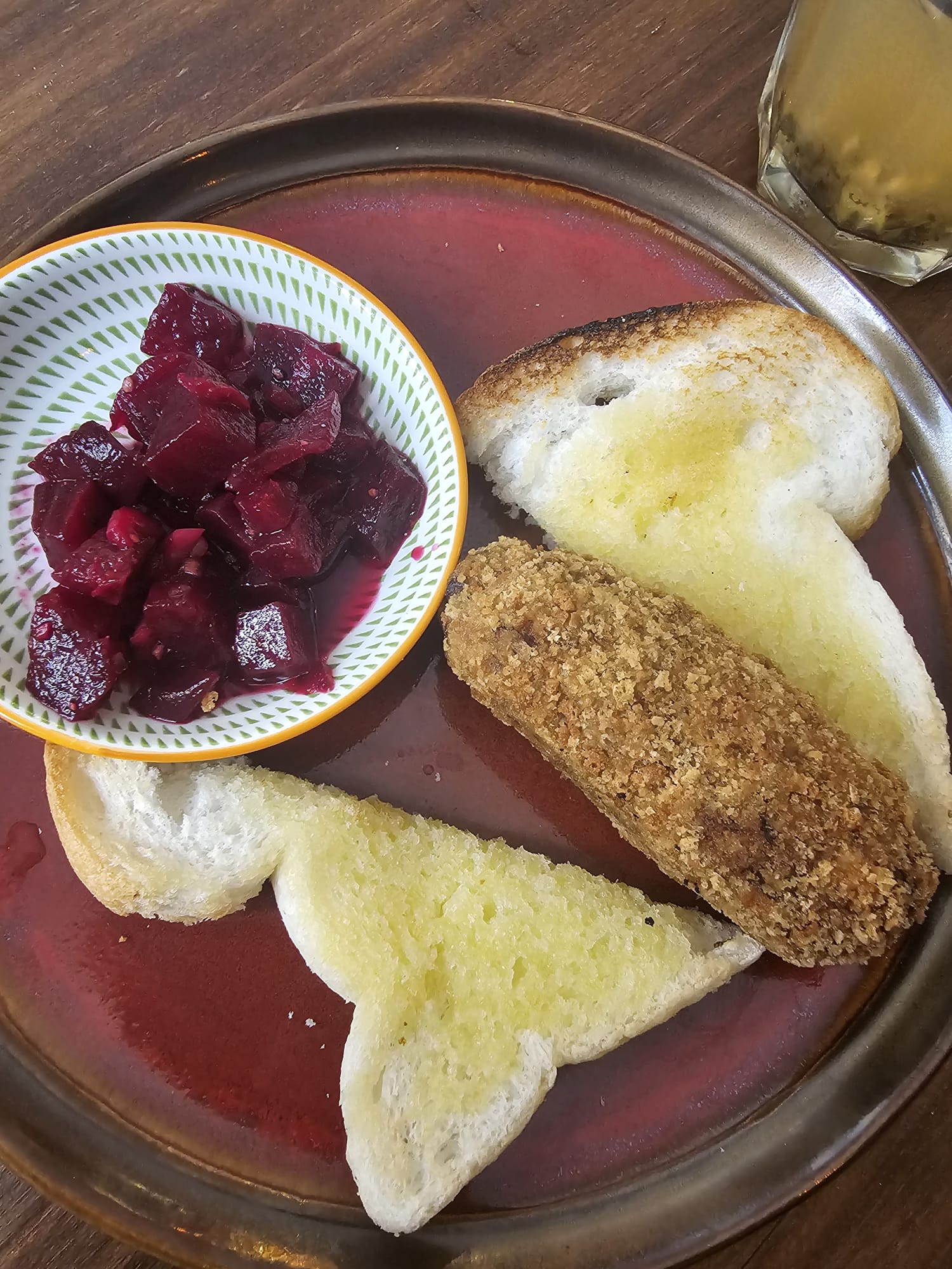 A small plate containing two slices of buttered gluten-free toast, a large golden-brown meat croquette, and a small side bowl of diced red beets.