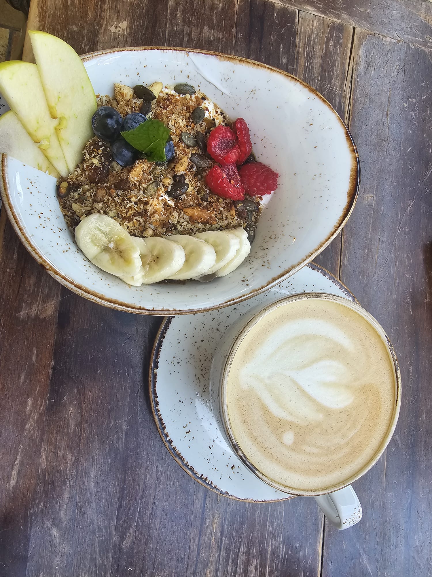 a yogurt bowl topped with banana slices and berries alongside a latte