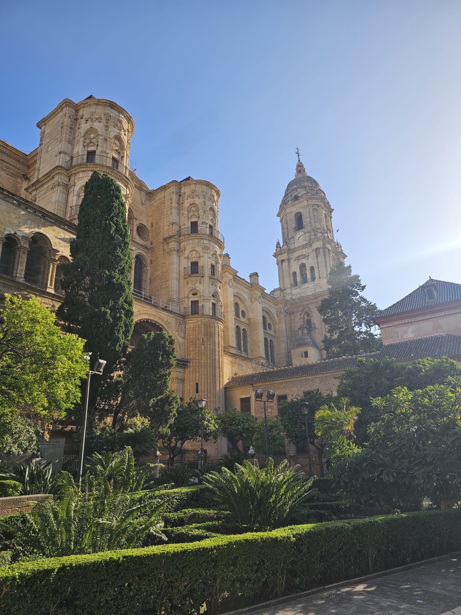 Málaga Cathedral surrounded by lush green gardens and trees against a bright blue sky