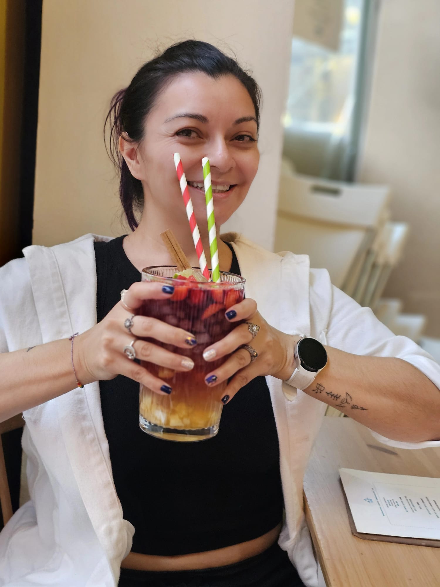 A woman smiling while holding a very large glass of red sangria filled with fruit and two striped straws.