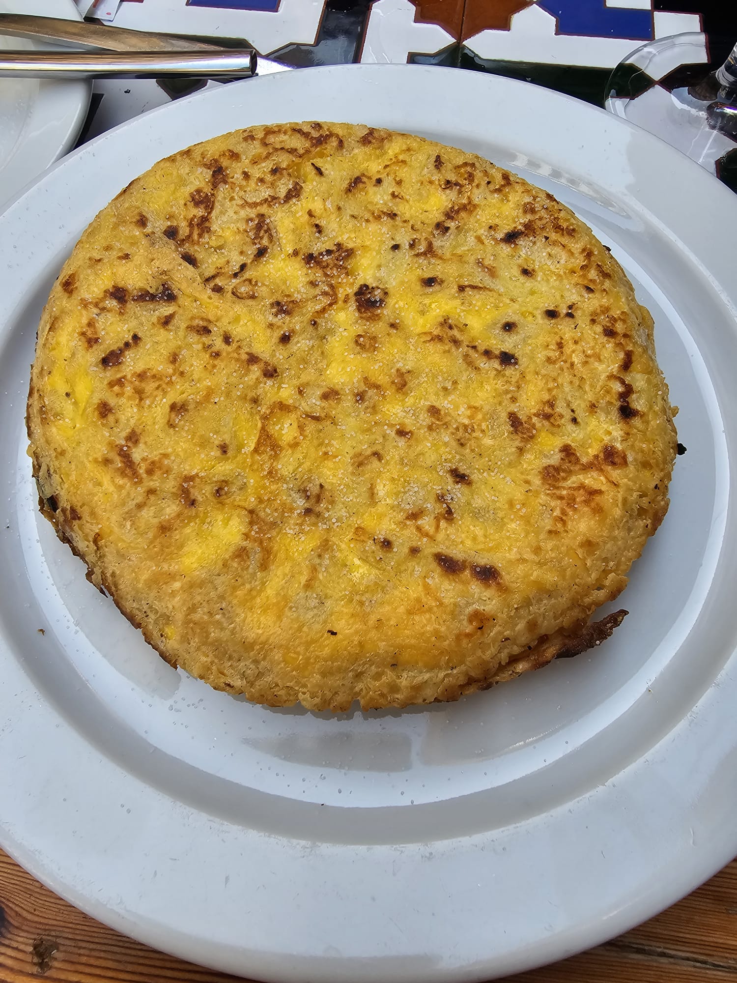 A top-down view of a classic Spanish tortilla (potato omelet), round and golden-brown, served on a white ceramic plate.