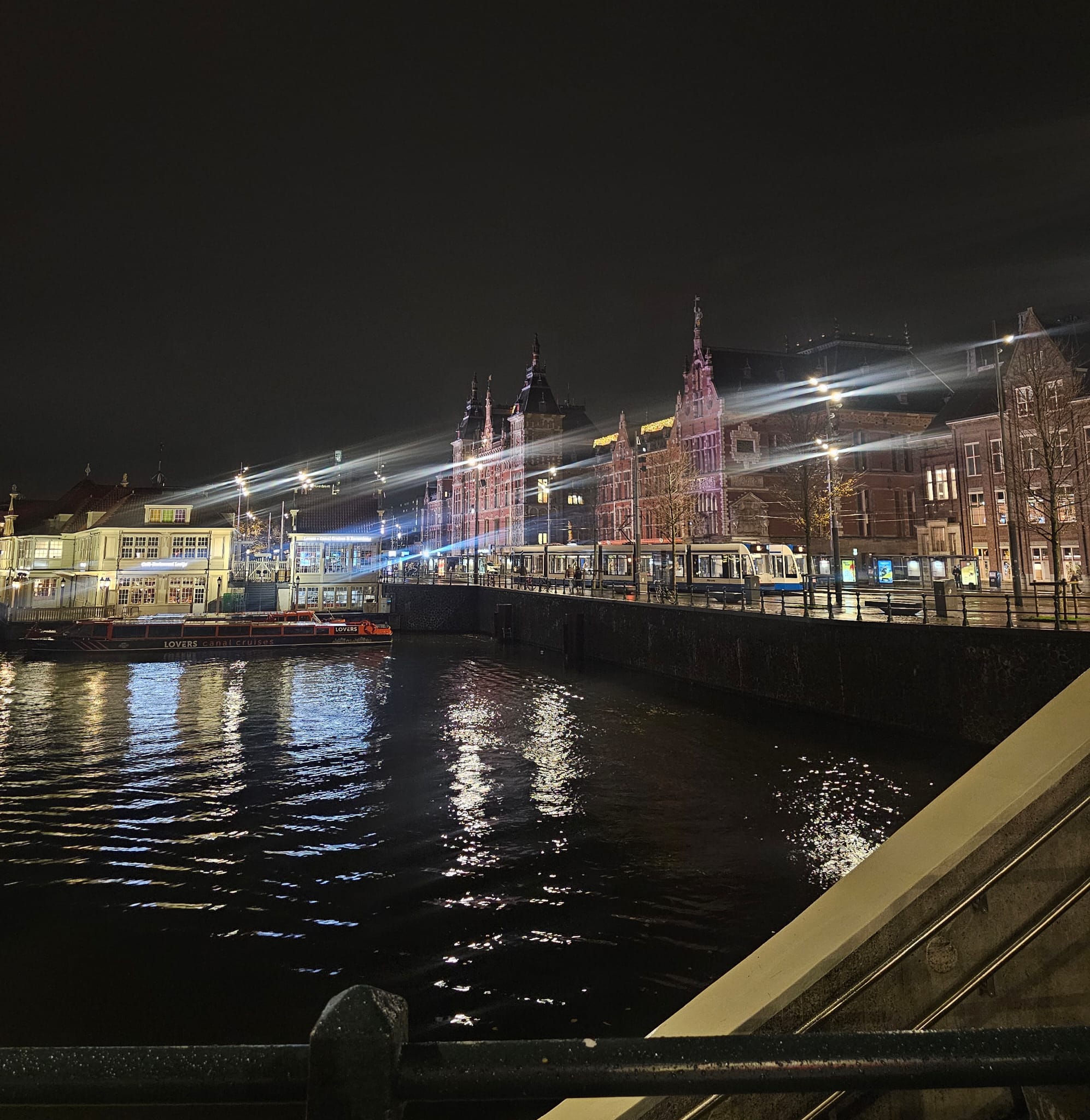 Blurry nighttime shot of Amsterdam's illuminated canals and bridges reflecting colorful lights in the water