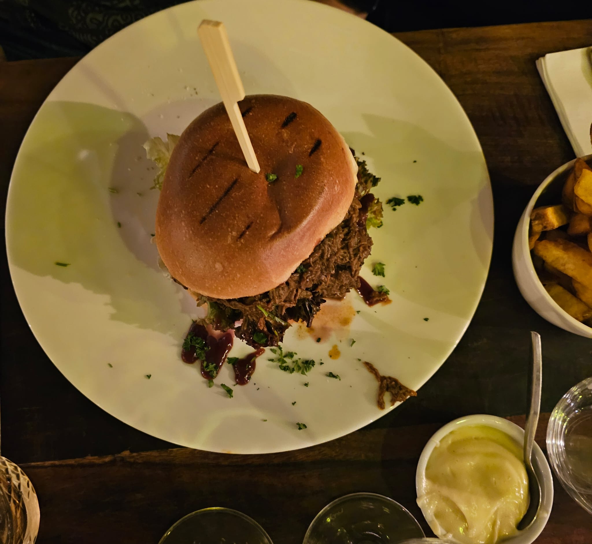 A gourmet beef burger with a shiny brioche bun, held together with a wooden skewer.