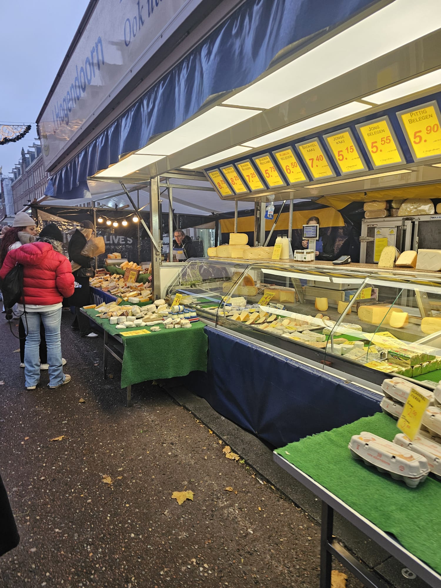 Outdoor cheese market stall with large rounds of Dutch cheese on display under bright lights in Amsterdam
