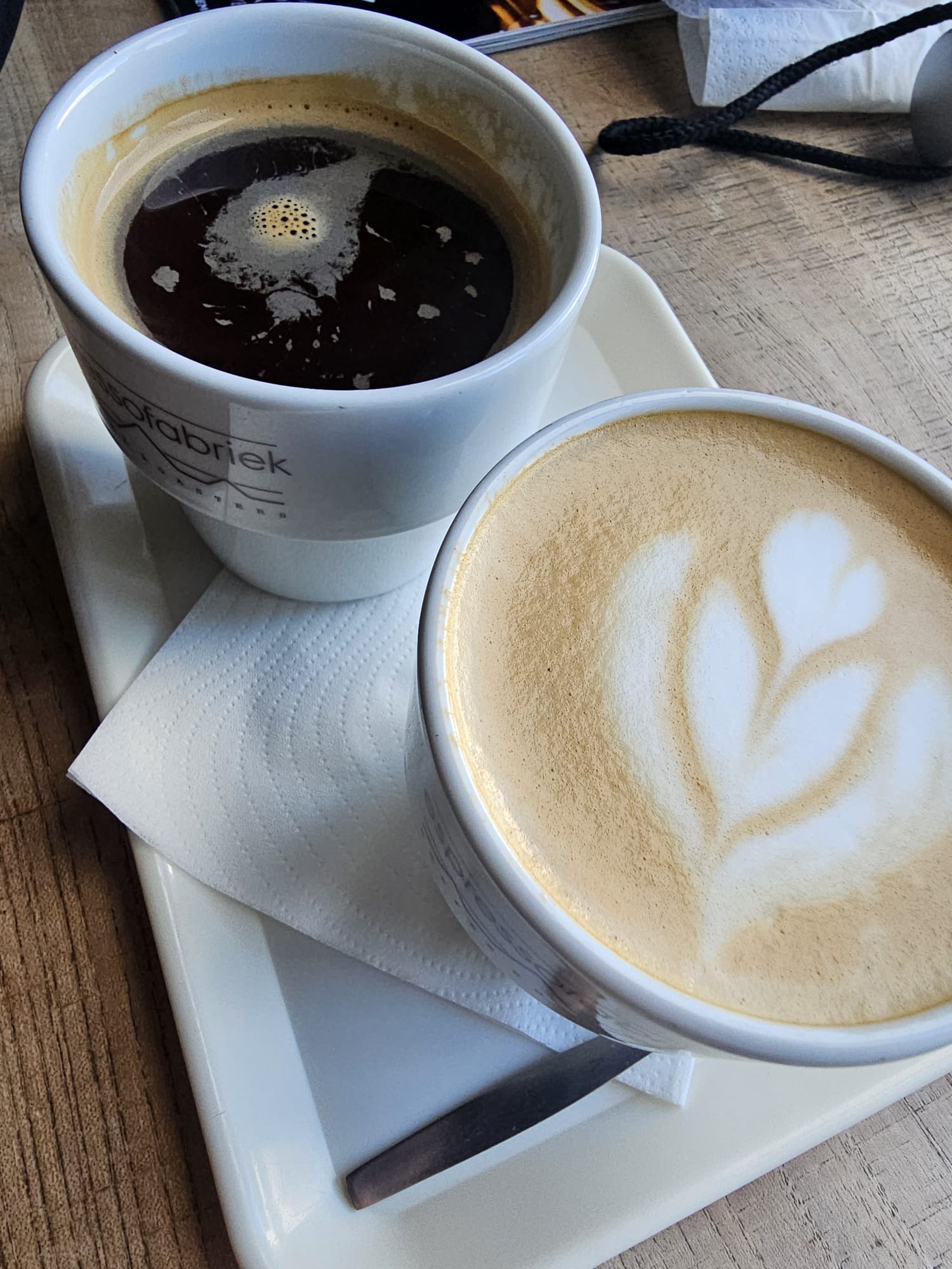A bird's-eye view of a white tray holding a classic black Americano and a creamy latte with leaf-patterned latte art.