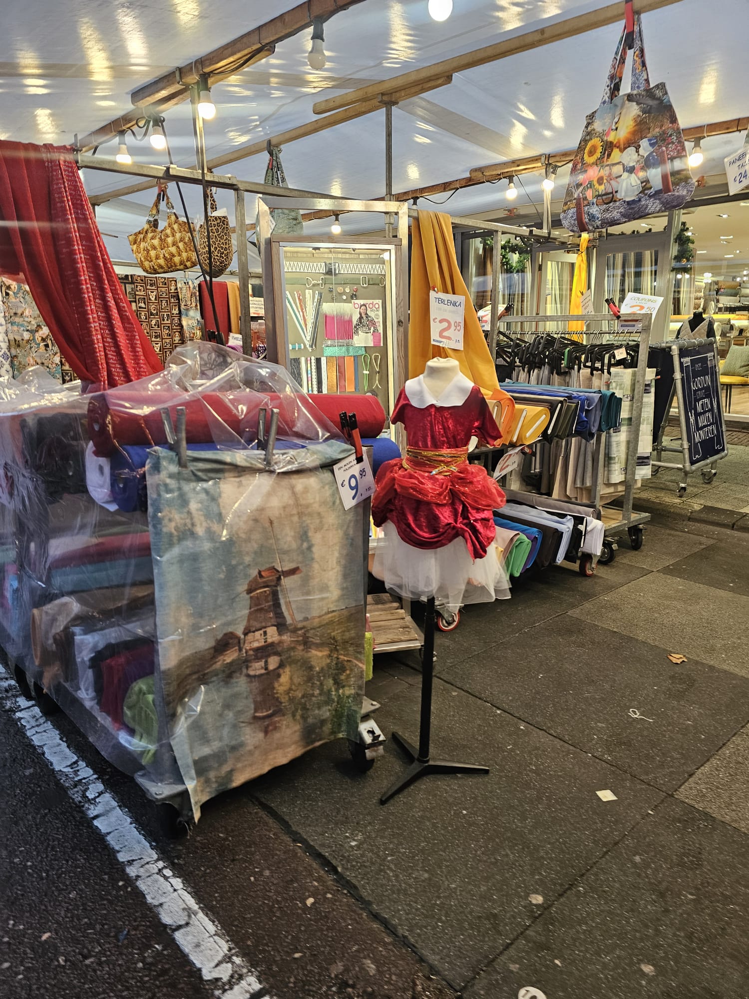 Outdoor fabric and clothing stall with bolts of colorful material and a dressed mannequin at an Amsterdam street market