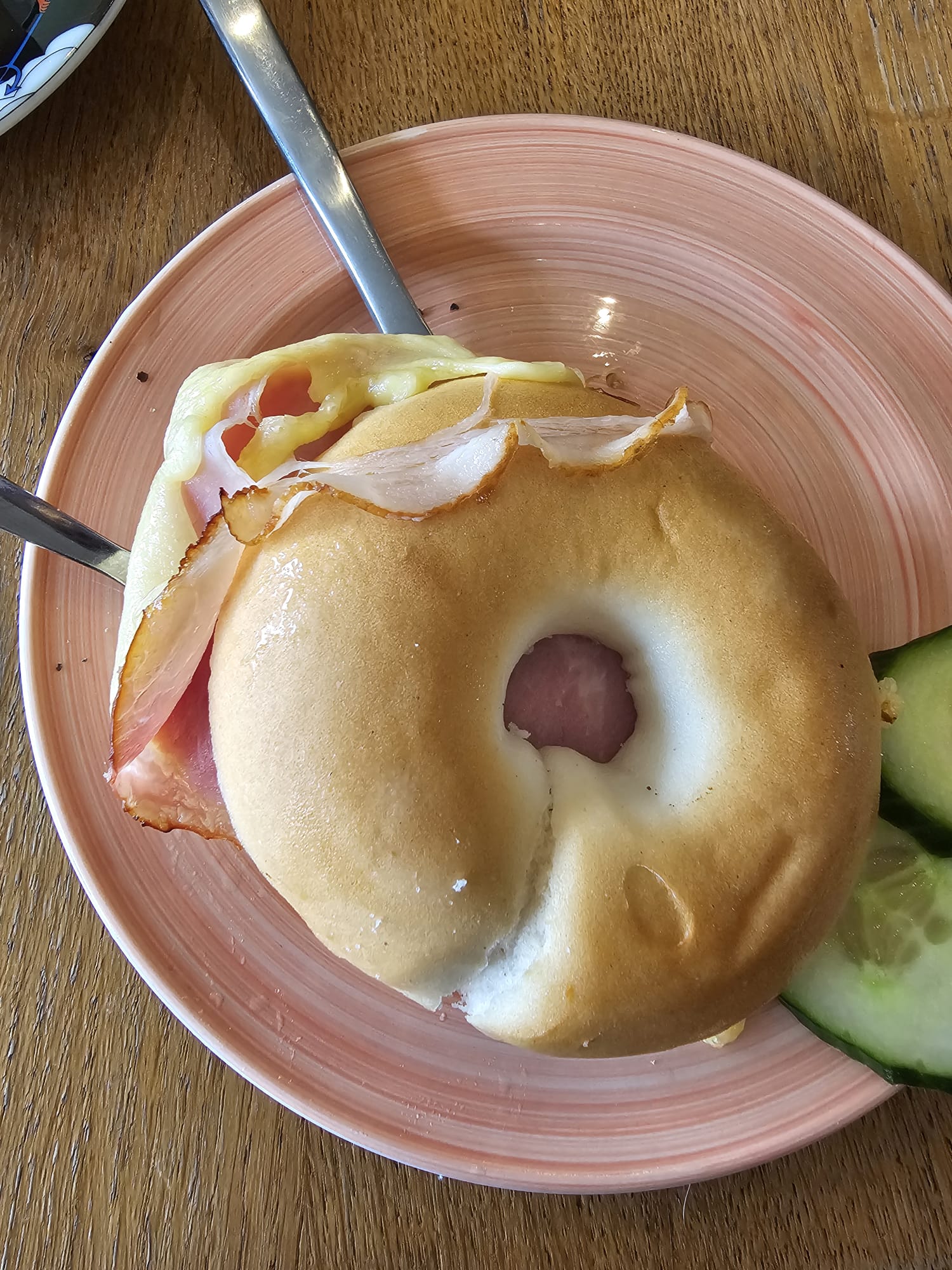 A gluten-free bagel toastie served on a pink plate, filled with melted cheese and a slice of ham.